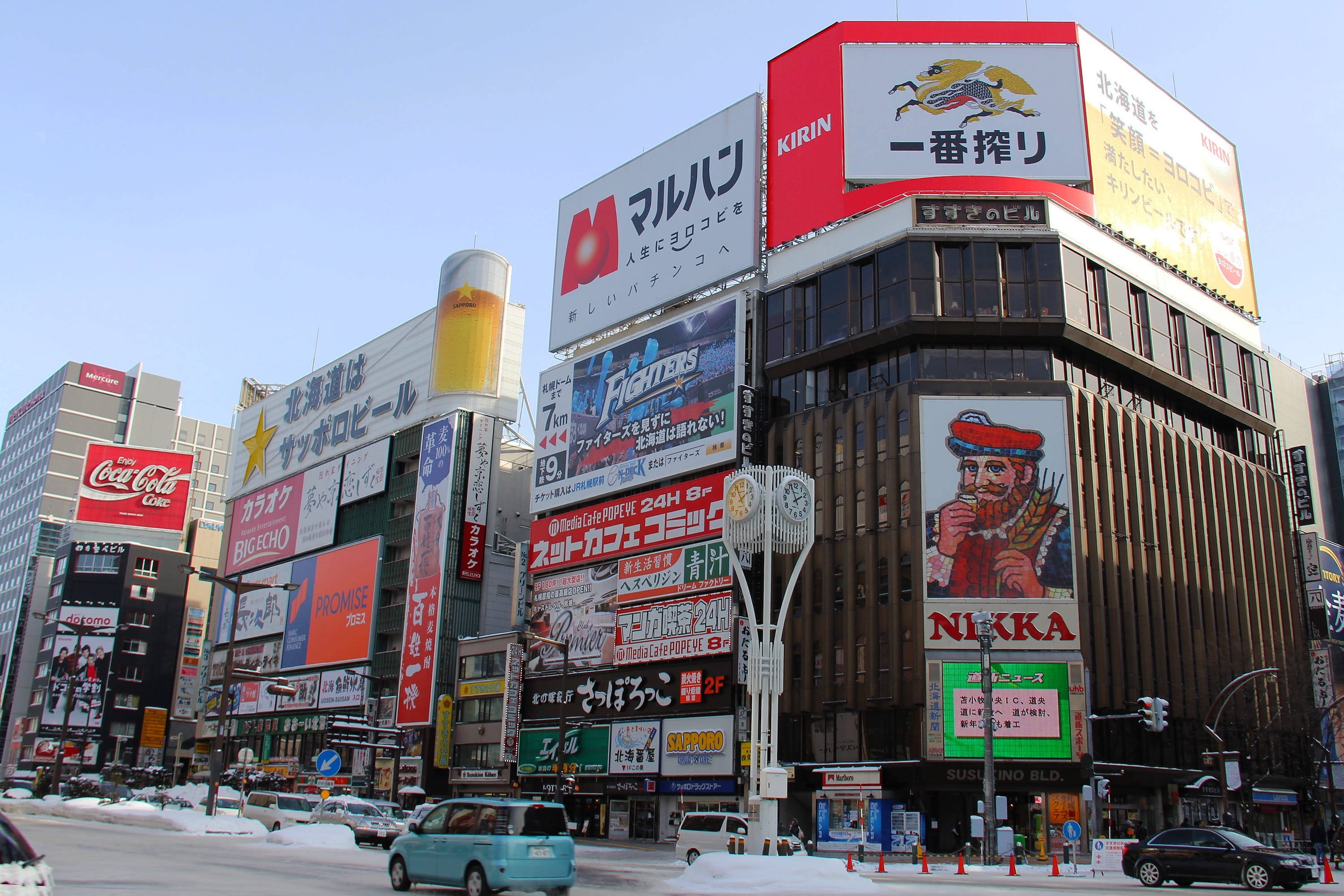 Mall 桌布 壁紙 — 白雪覆蓋著一條繁華的日本城市街道，兩旁是高聳的建築物，上面掛滿了色彩繽紛的霓虹招牌和廣告，在清澈的藍天下。