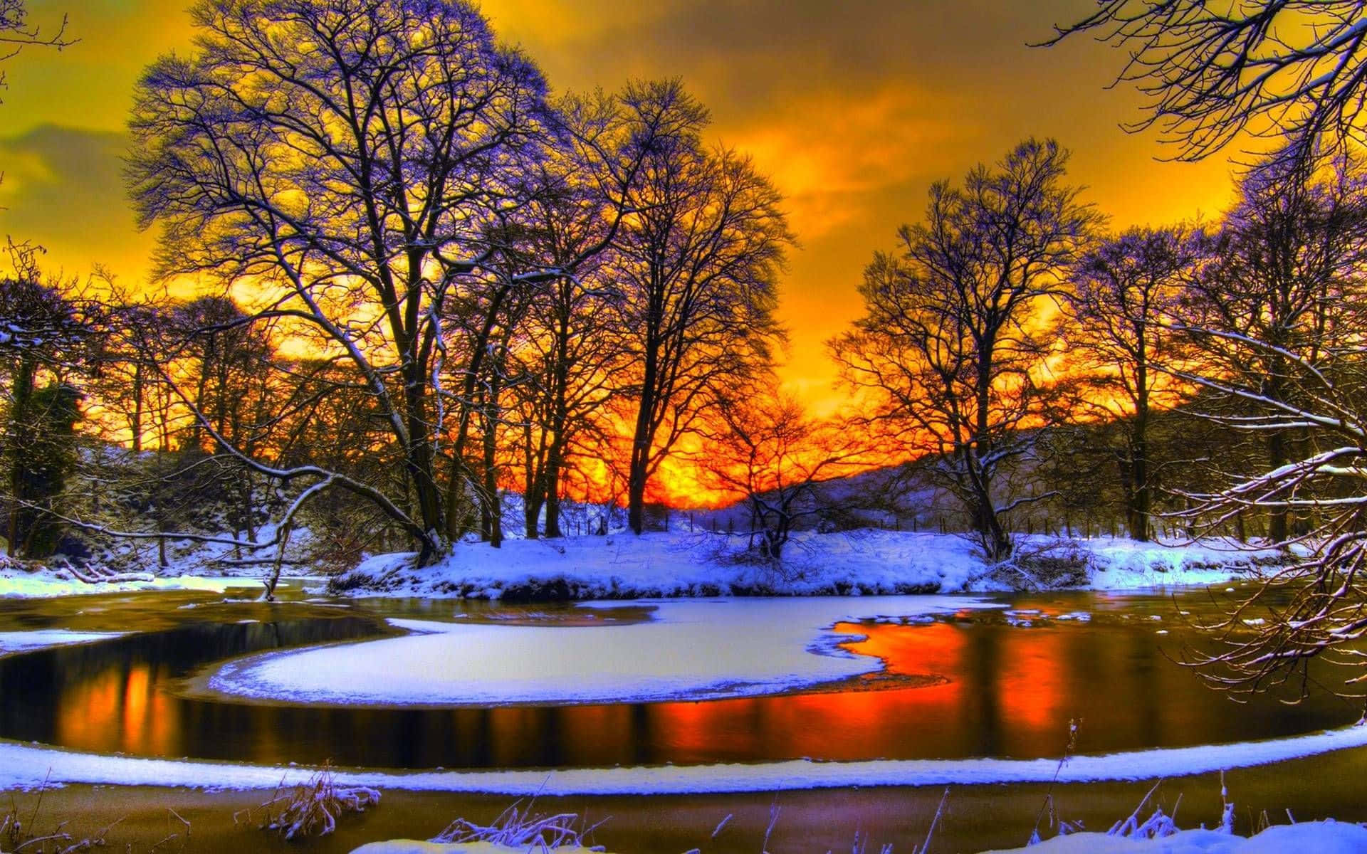 Winter Sunset 桌布 壁紙 — 白雪覆蓋著光禿禿的樹木，旁邊是一條結冰的河流，映照著火紅橙色的日落天空。