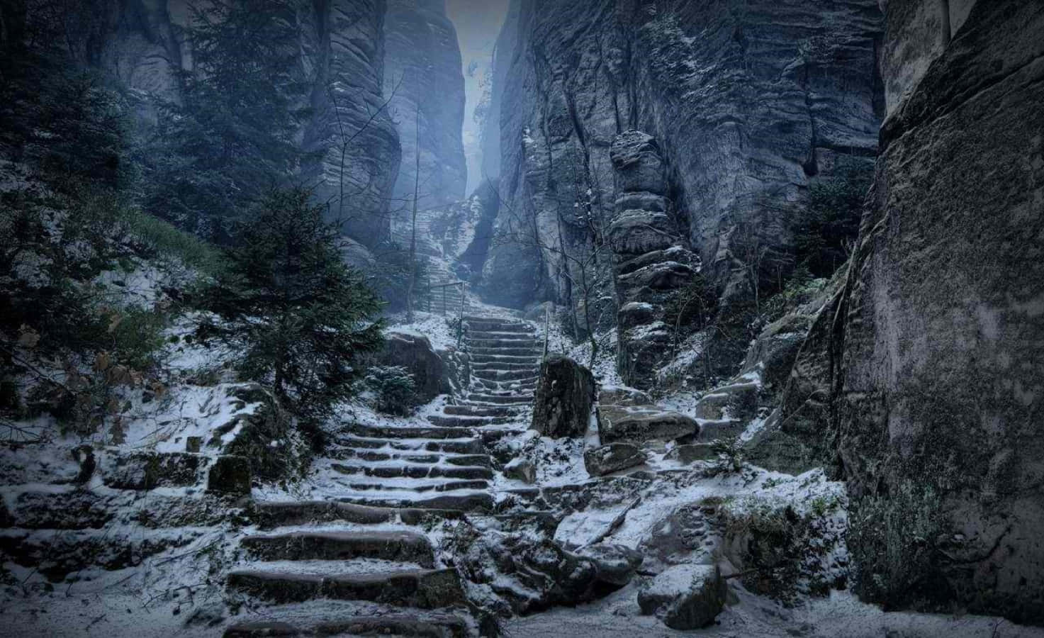 Skyrim Landscapes 桌布 壁紙 — 白雪覆蓋著古老石階，蜿蜒穿過高聳霧氣繚繞的懸崖，在令人難忘的冬日森林中。