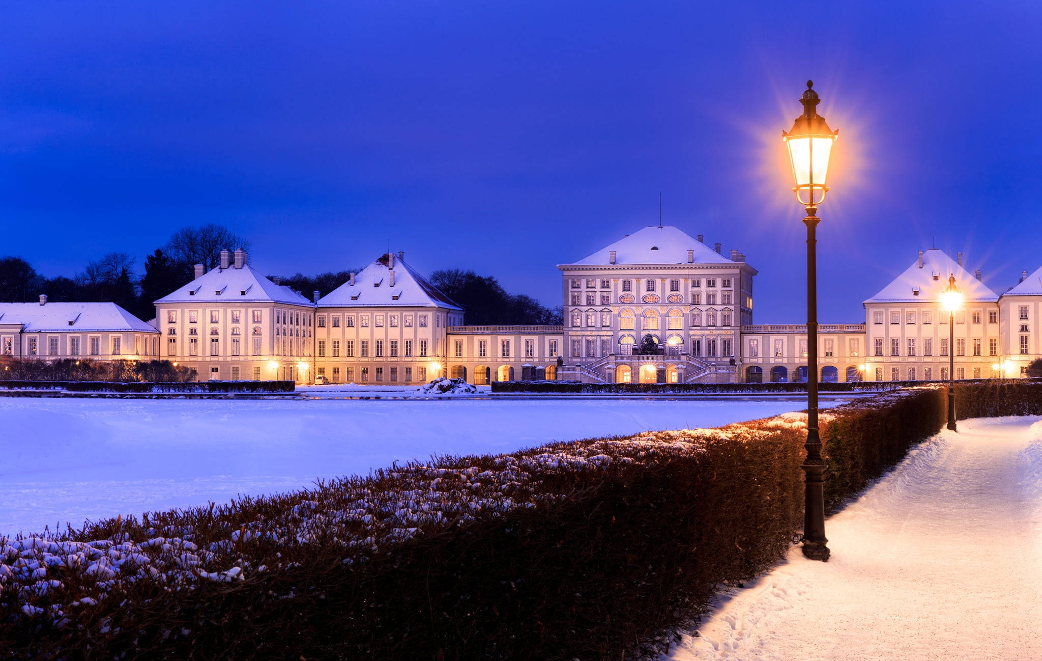 Munich 桌布 壁紙 — 白雪覆蓋著宏偉的宮殿建築群，在深藍色的暮色天空下，溫暖的街燈照亮了一切。