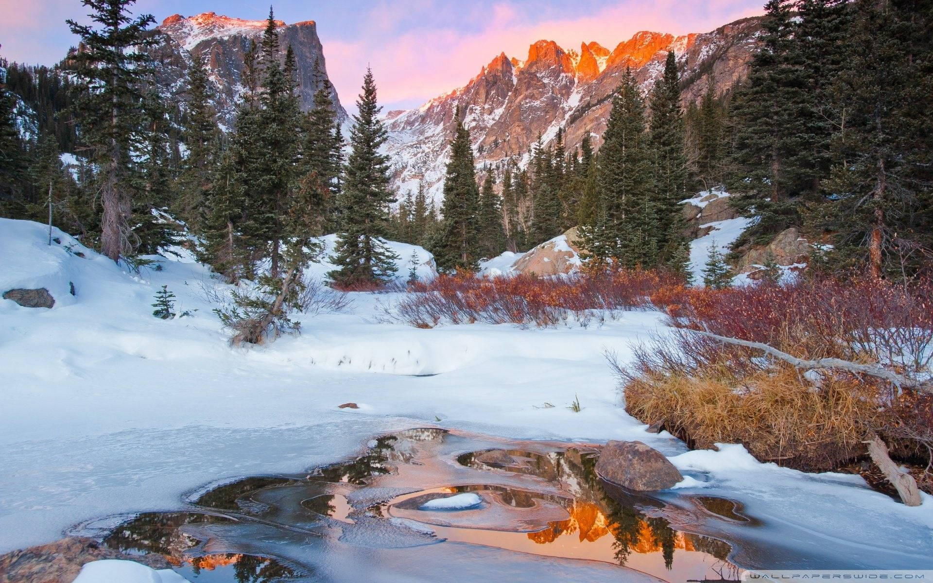 Rocky Mountain National Park 桌布 壁紙 — 白雪覆蓋著山谷，金色的夕陽照耀著崎嶇的山峰和常綠樹，溫暖的色調倒映在冰冷的溪流中。