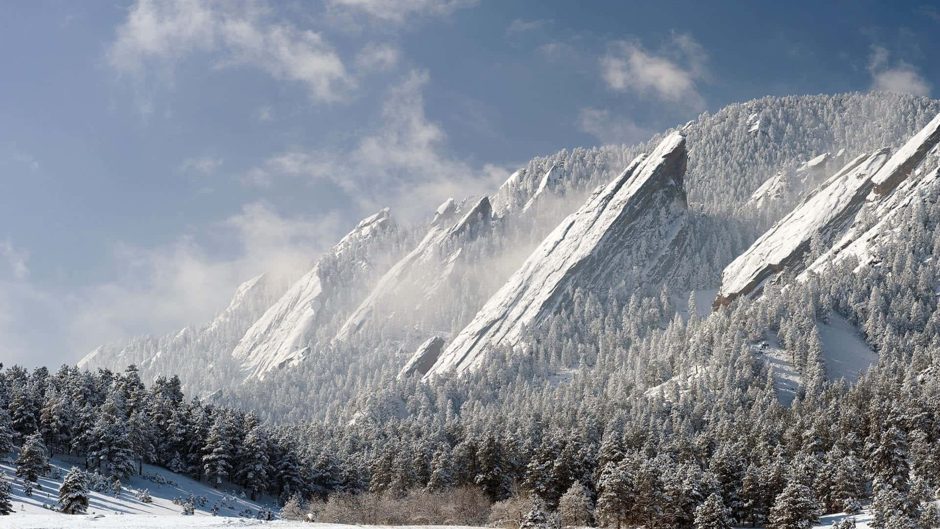 Colorado Mountains 桌布 壁紙 — 白雪覆蓋著崎嶇的山峰和常綠樹，天空湛藍明亮，飄著縷縷薄雲。