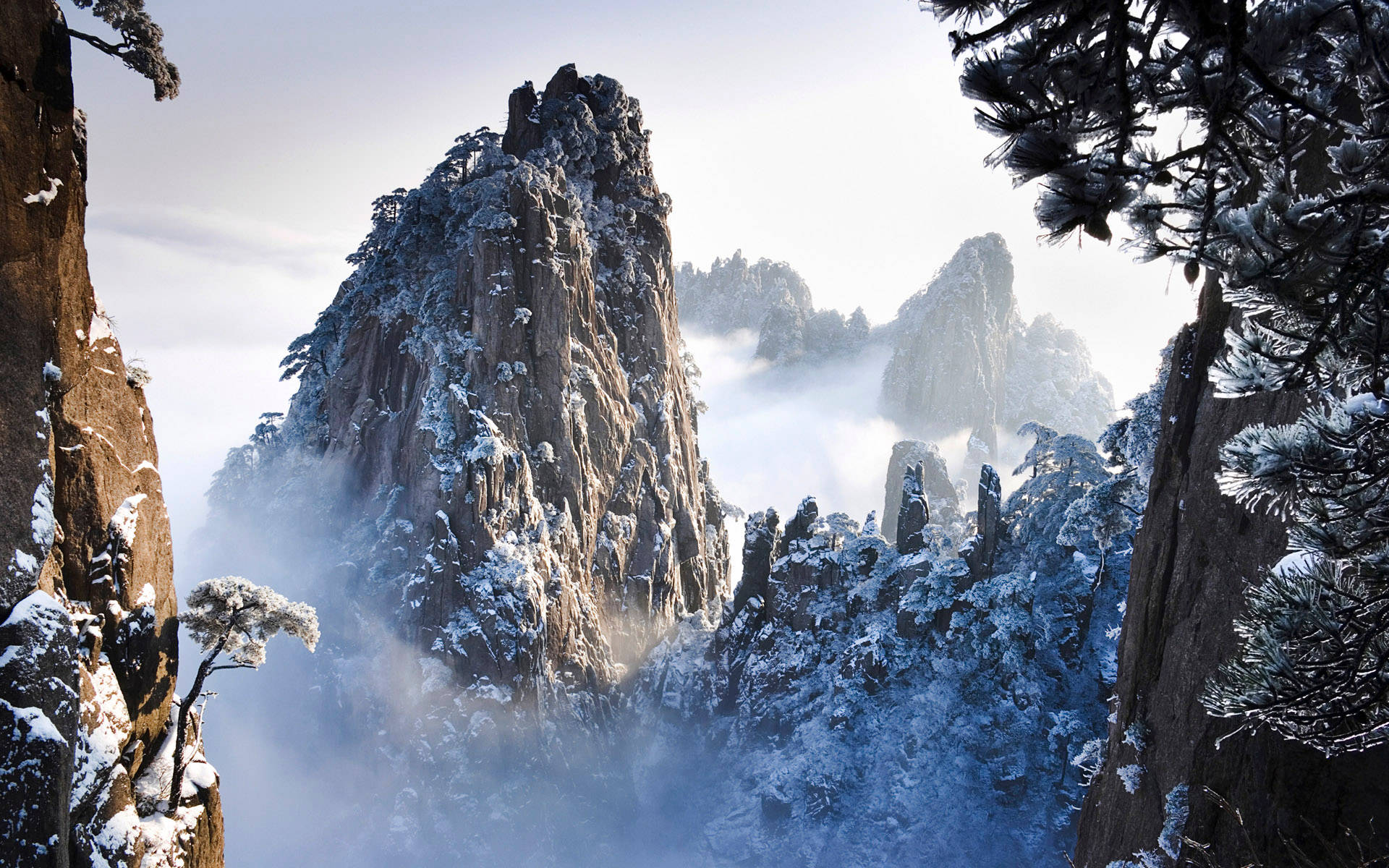 雪山 桌布 壁紙 — 白雪覆蓋著崎嶇的山峰和松樹，薄霧在山谷中盤旋。