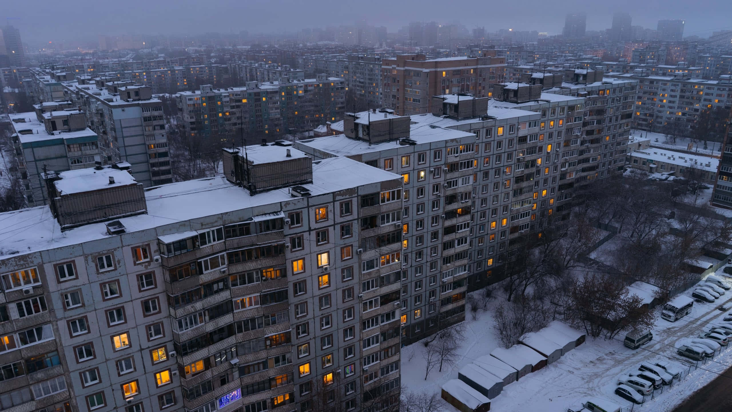 Russian 桌布 壁紙 — 白雪覆蓋著廣闊的都市公寓群，溫暖的燈光從窗戶中透出，映照著灰色的冬日黃昏。