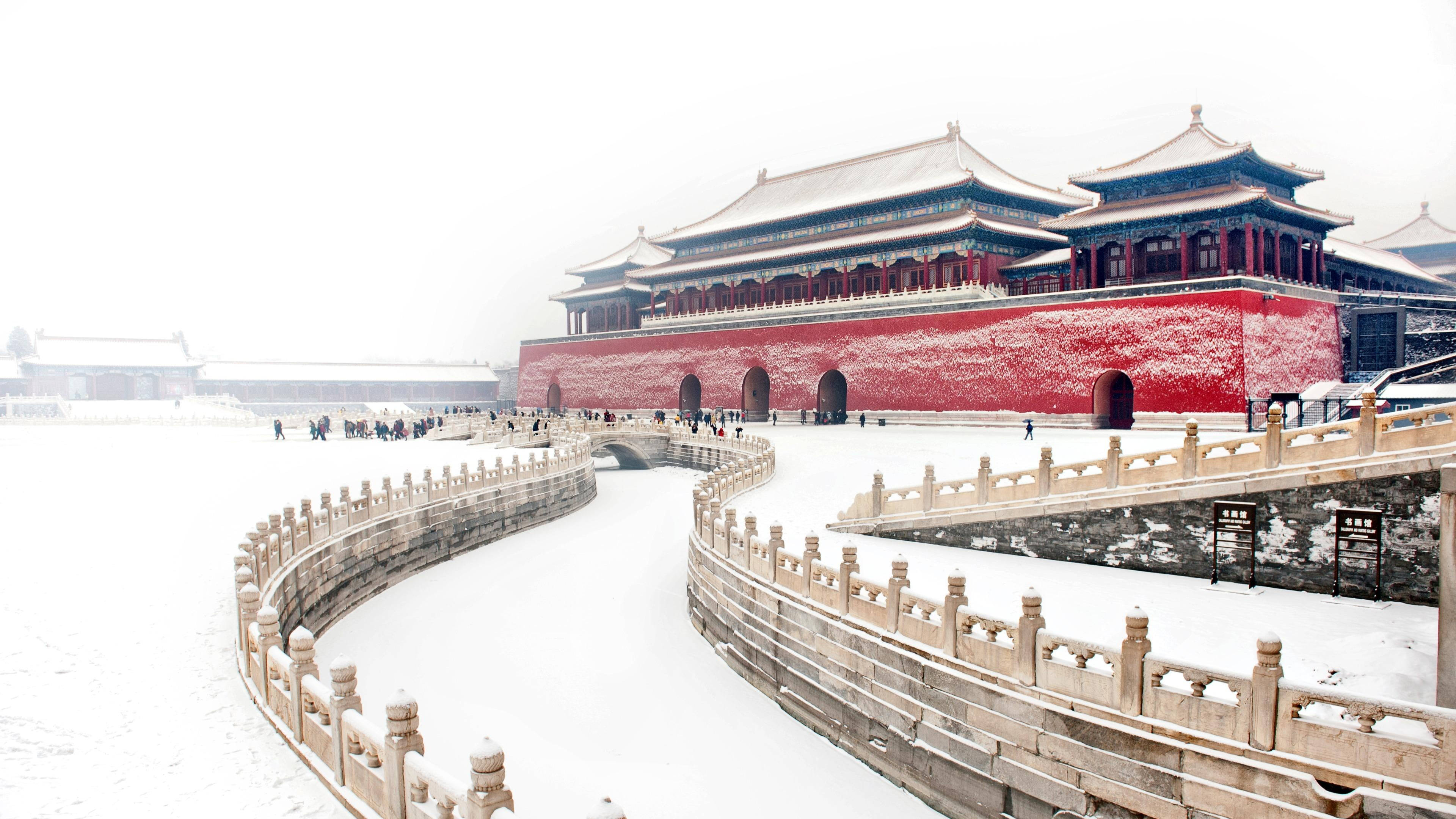 雪 桌布 壁紙 — 白雪覆蓋著故宮標誌性的紅牆和石橋，在朦朧的冬日天空下。
