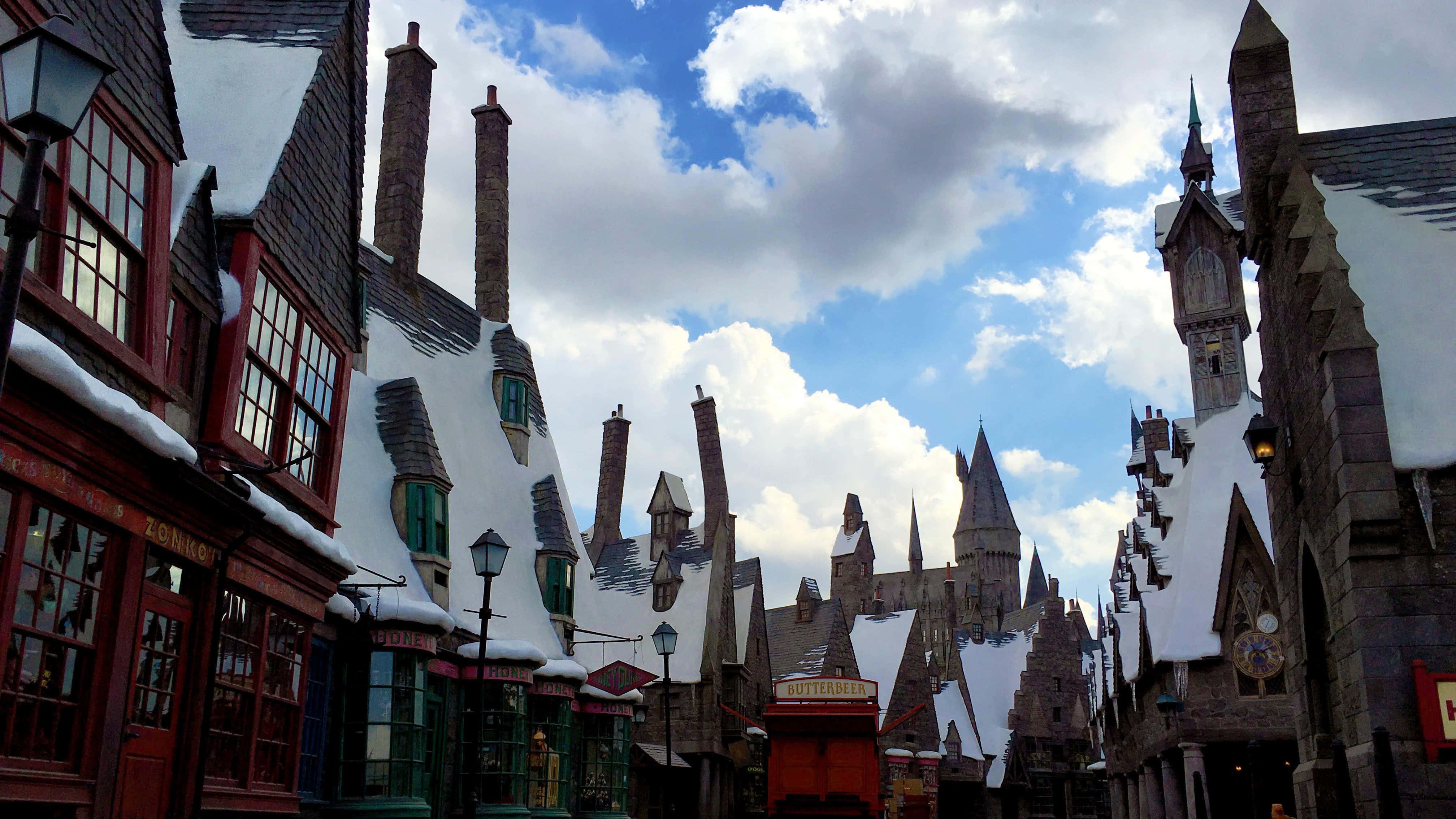 Wizarding World 桌布 壁紙 — 白雪覆蓋著斜角巷彎曲的屋頂和煙囪，天空湛藍，白雲蓬鬆。