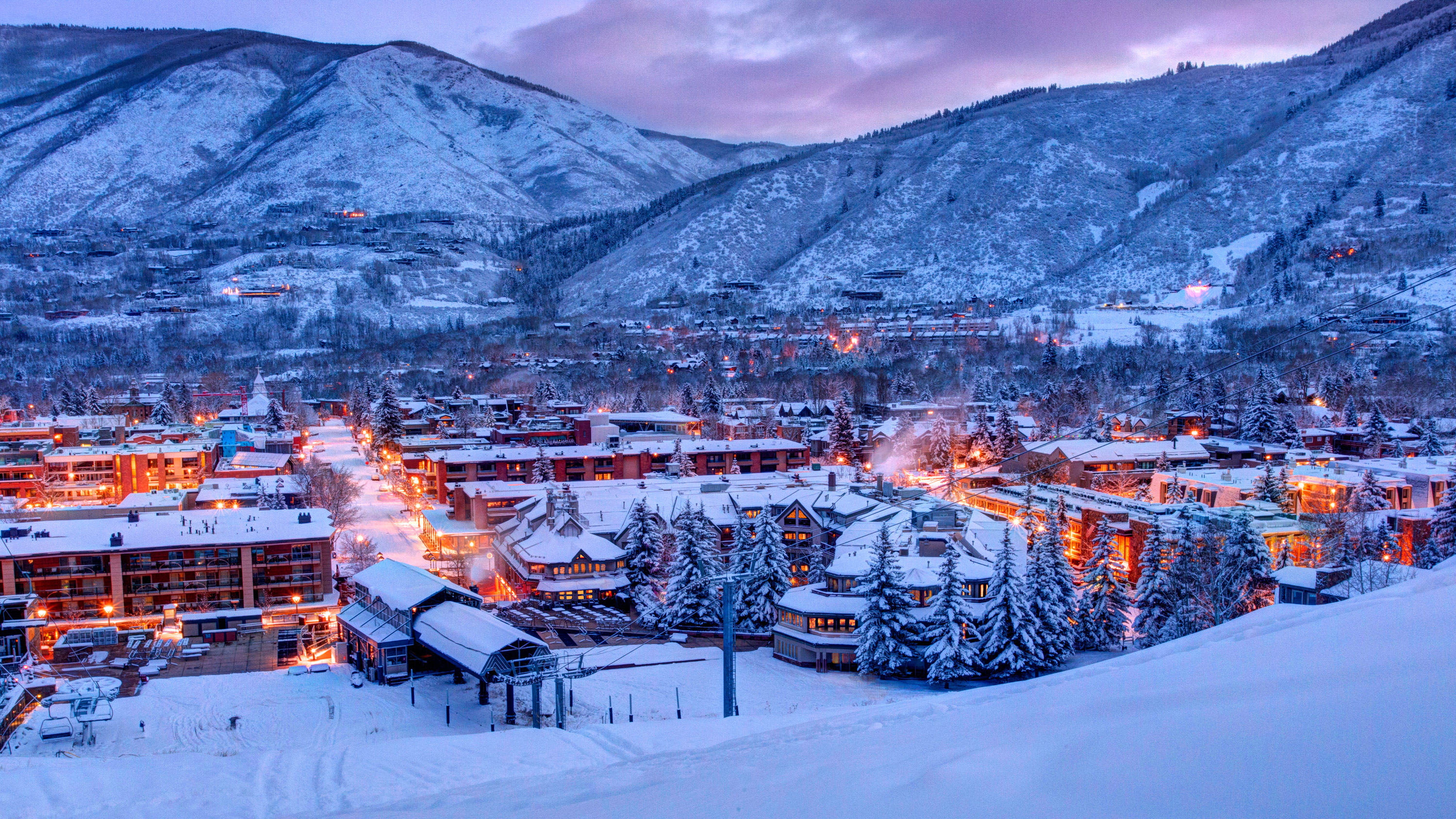 Colorado 桌布 壁紙 — 白雪覆蓋著暮色中的山城，建築物和樹木的燈光在紫色天空下閃爍。