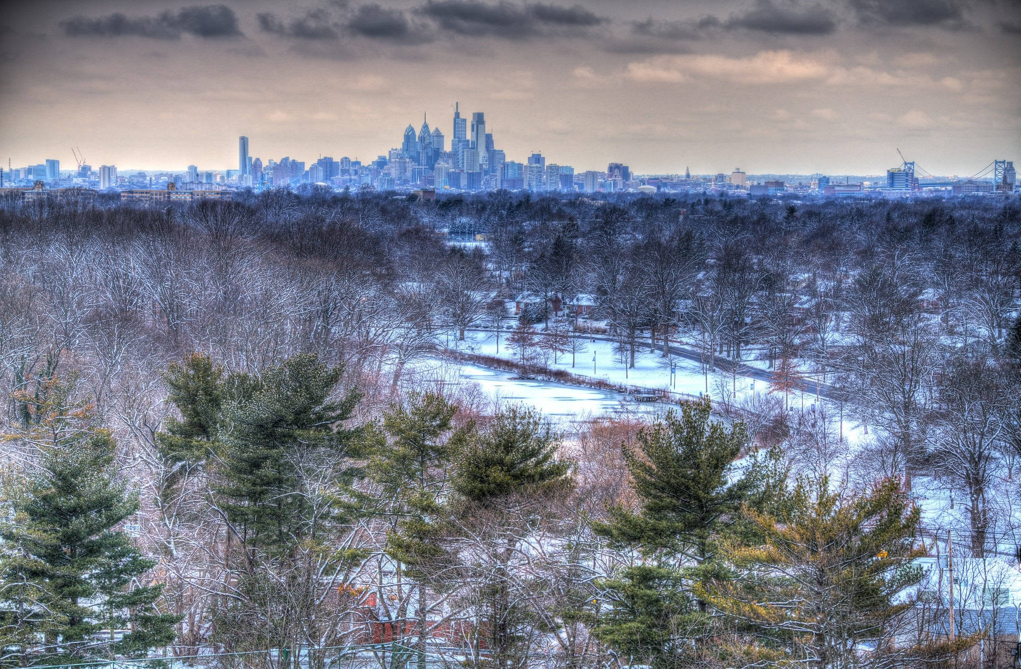 Philadelphia 桌布 壁紙 — 白雪覆蓋著樹木繁茂的公園，遠處的城市天際線在陰沉多雲的天空下升起。