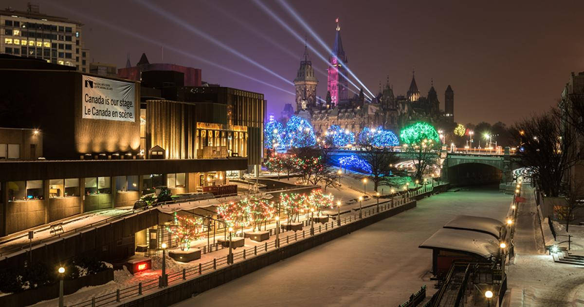 聖誕燈飾 桌布 壁紙 — 白雪覆蓋著渥太華一個充滿活力的冬夜，色彩繽紛的燈光照亮了國會山附近的樹木和建築物。
