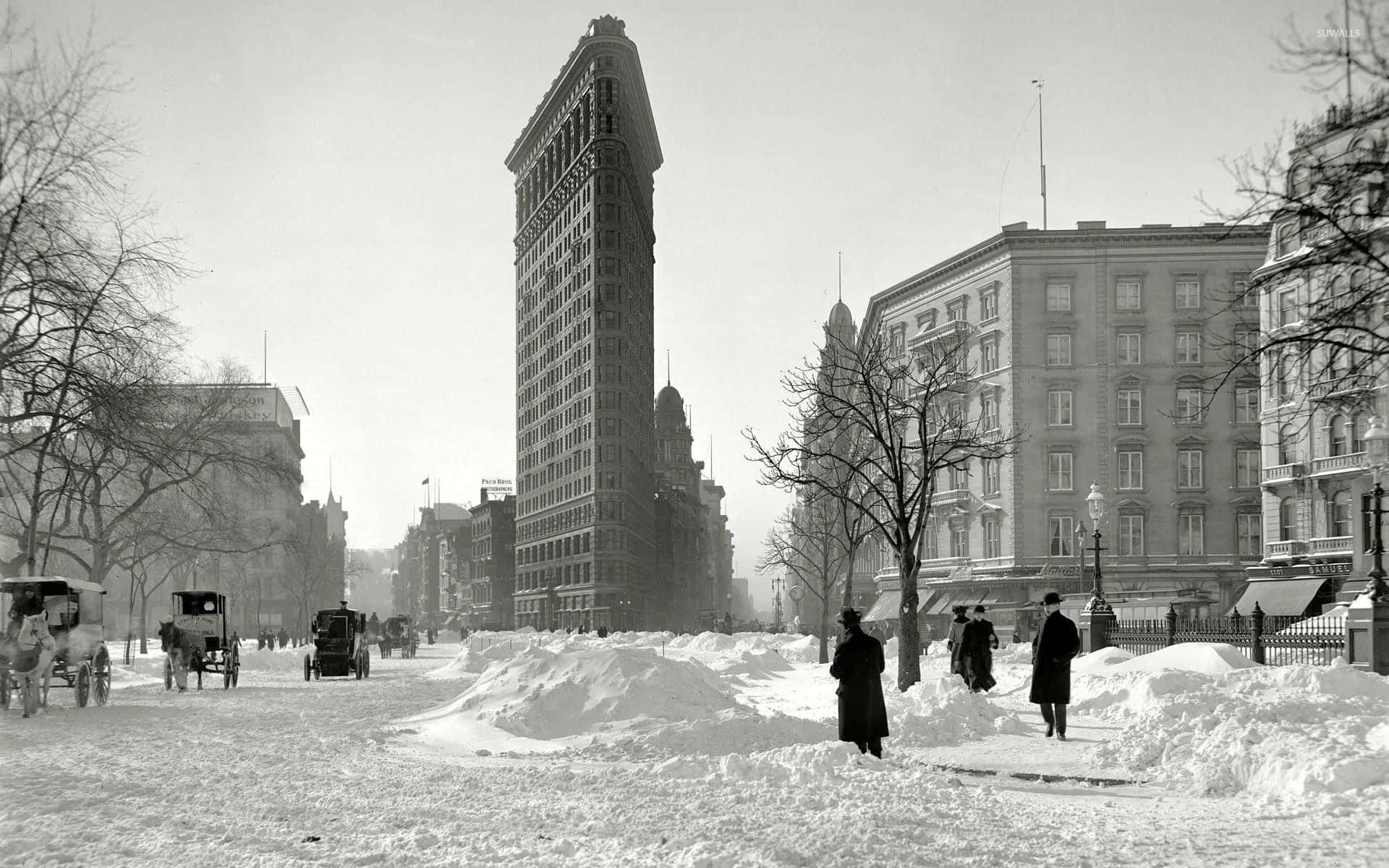 New York 桌布 壁紙 — 白雪覆蓋著繁忙的城市街道，行人與馬車在冬季經過標誌性的熨斗大廈。