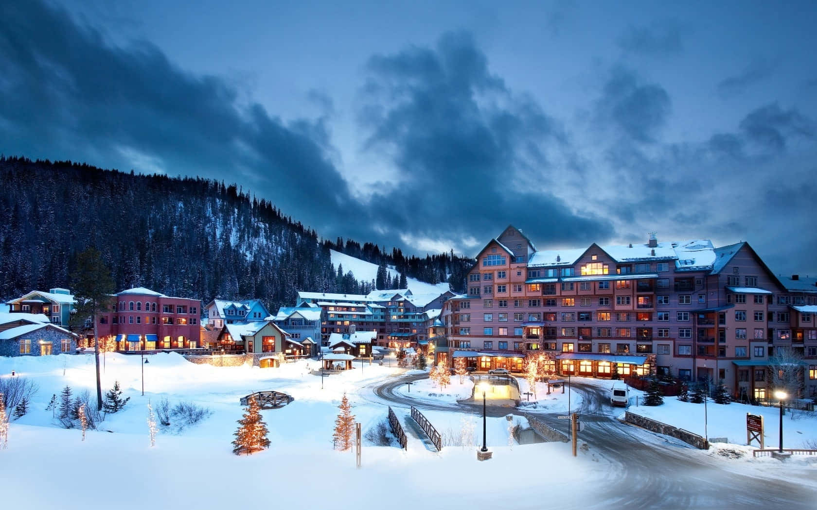 Ski Resort 桌布 壁紙 — 白雪覆蓋著黃昏時分舒適的山村，溫暖的燈光從窗戶透出，映襯著陰沉的天色。