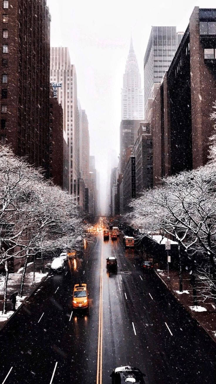 Vsco 桌布 壁紙 — 白雪覆蓋高聳的城市摩天大樓，黃色計程車在灰色冬日天空下沿著濕漉漉的大道滑行。