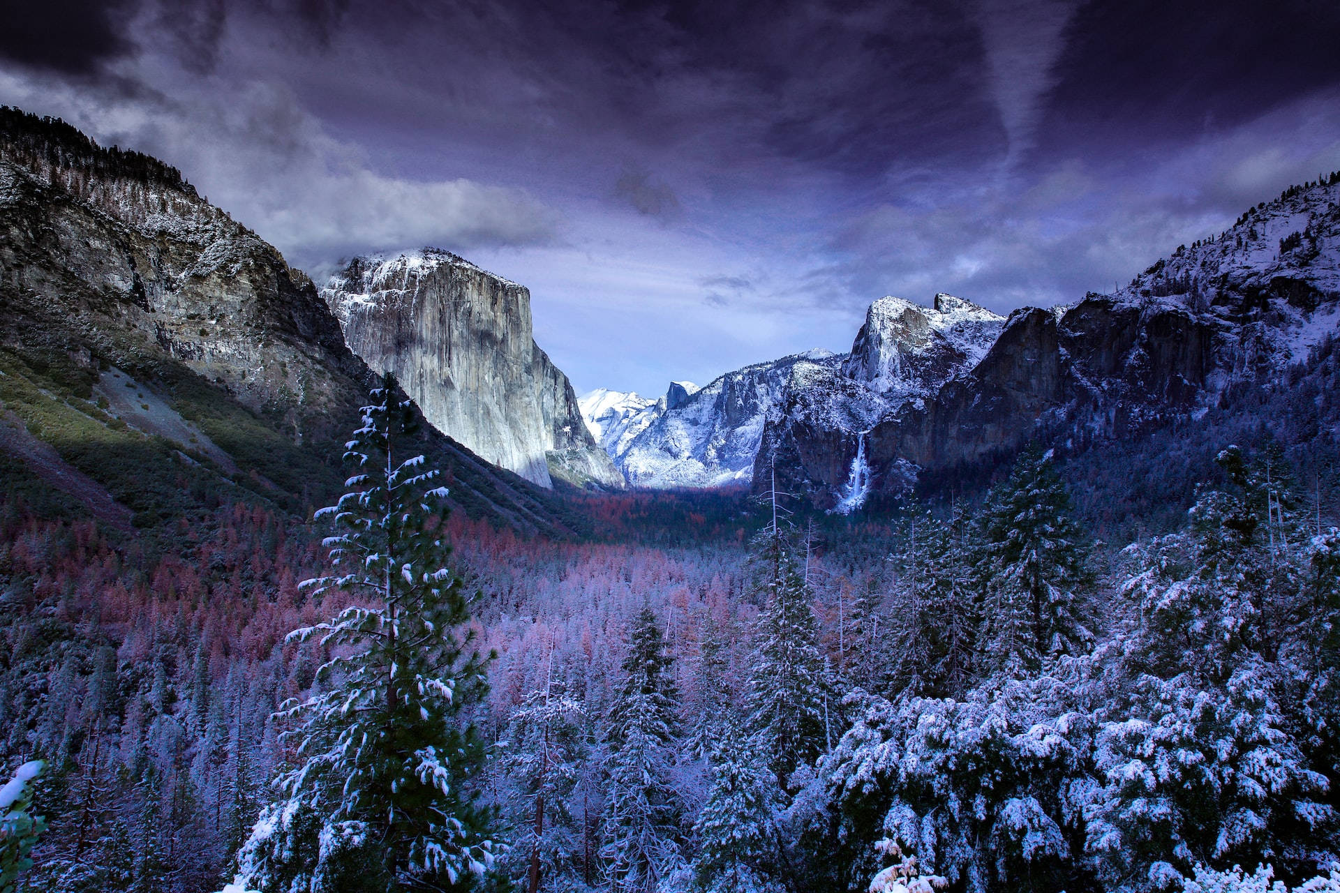 Mountain Landscape 桌布 壁紙 — 白雪覆蓋高聳的花崗岩懸崖和常綠樹，在戲劇性的紫色暮色天空下。