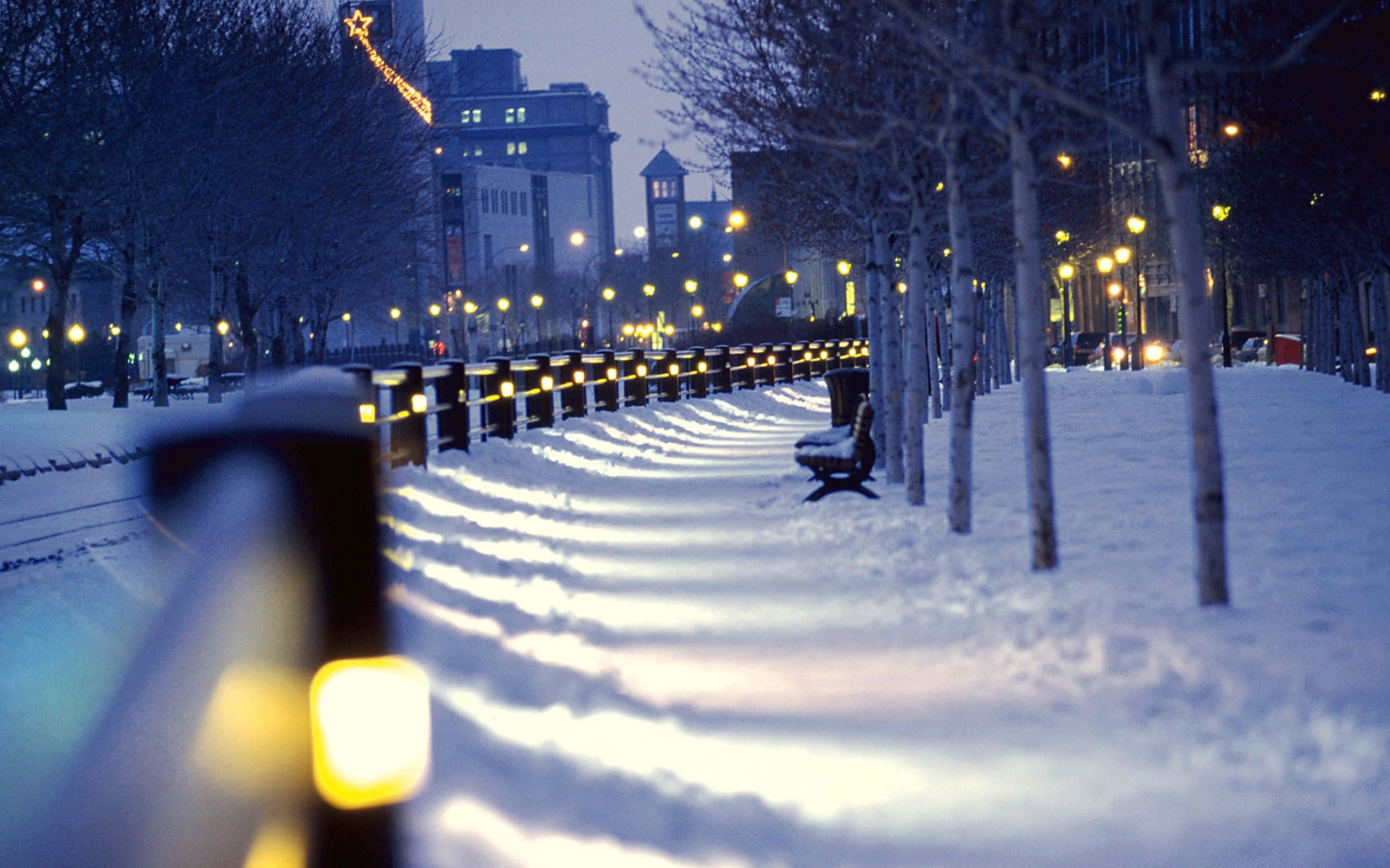 Snowy Christmas 桌布 壁紙 — 白雪覆蓋黃昏時分的城市公園，發光的街燈在小徑和光禿禿的樹木上投射出溫暖的倒影。