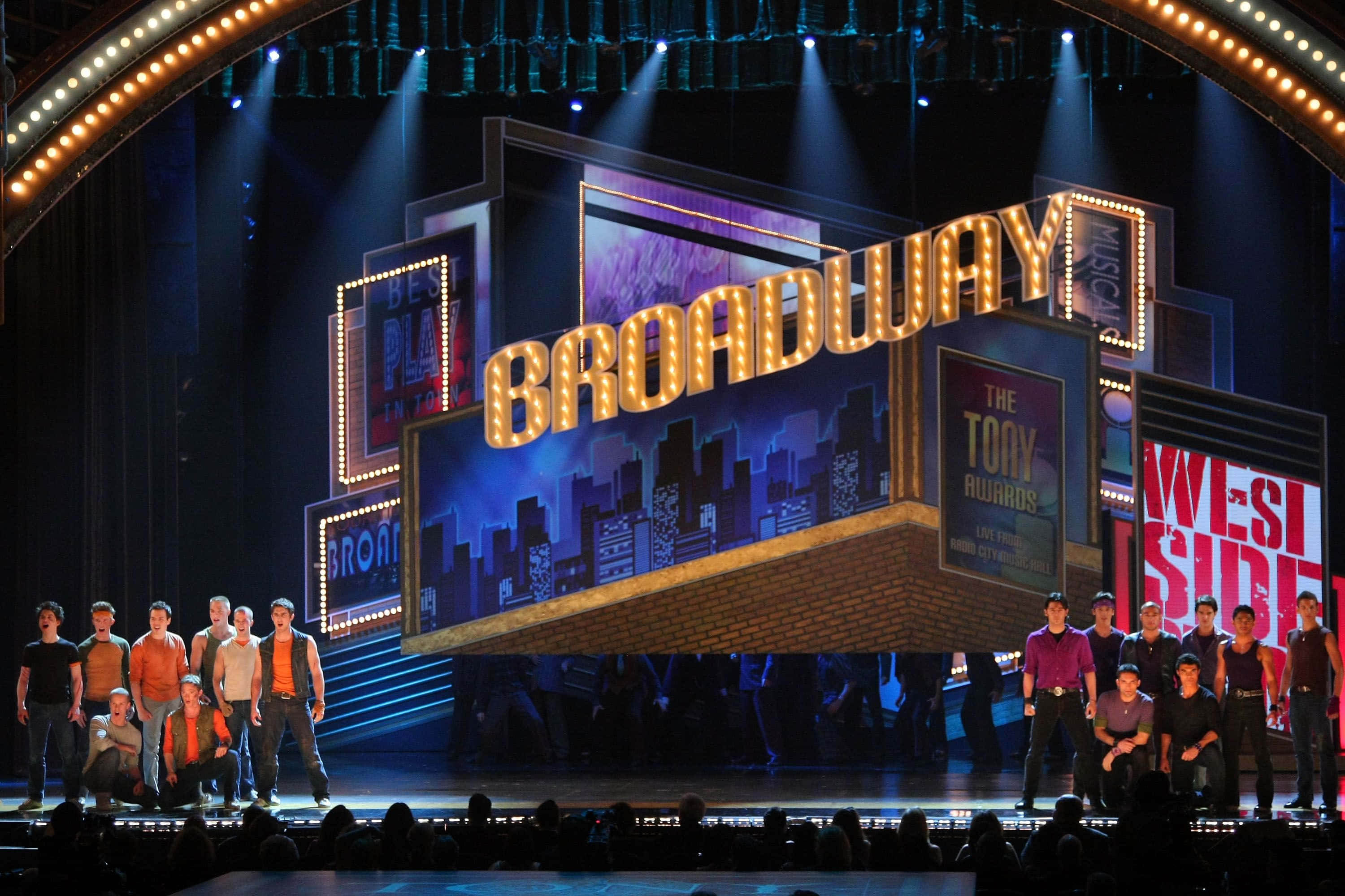 show 桌布 壁紙 — 百老匯舞台被聚光燈照亮，表演者在巨大的發光「BROADWAY」標誌和「TONY AWARDS」背景前擺姿勢。