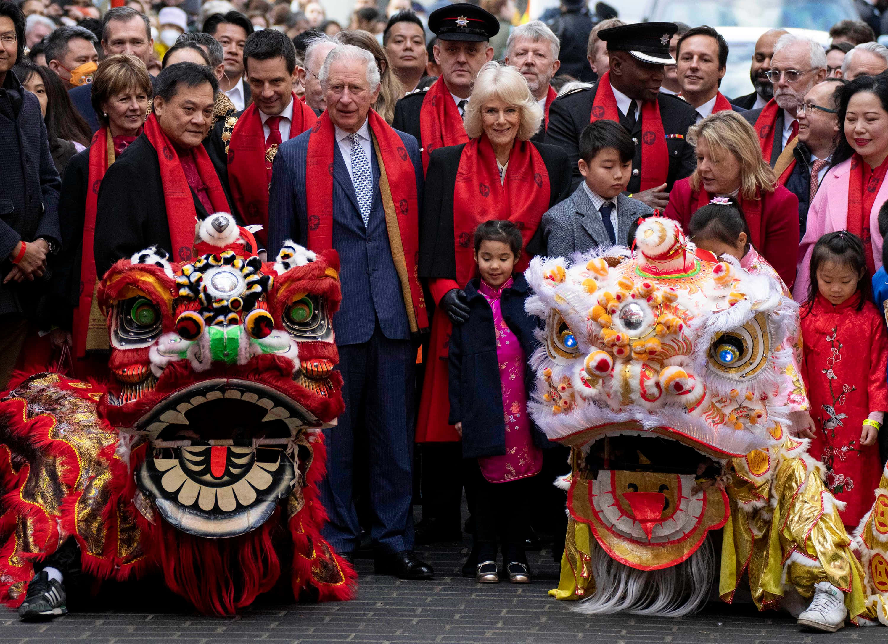 Chinese New Year 2022 桌布 壁紙 — 皇室夫婦微笑站在鮮豔的紅色和金色舞獅服裝旁，參加節日公眾慶祝活動。