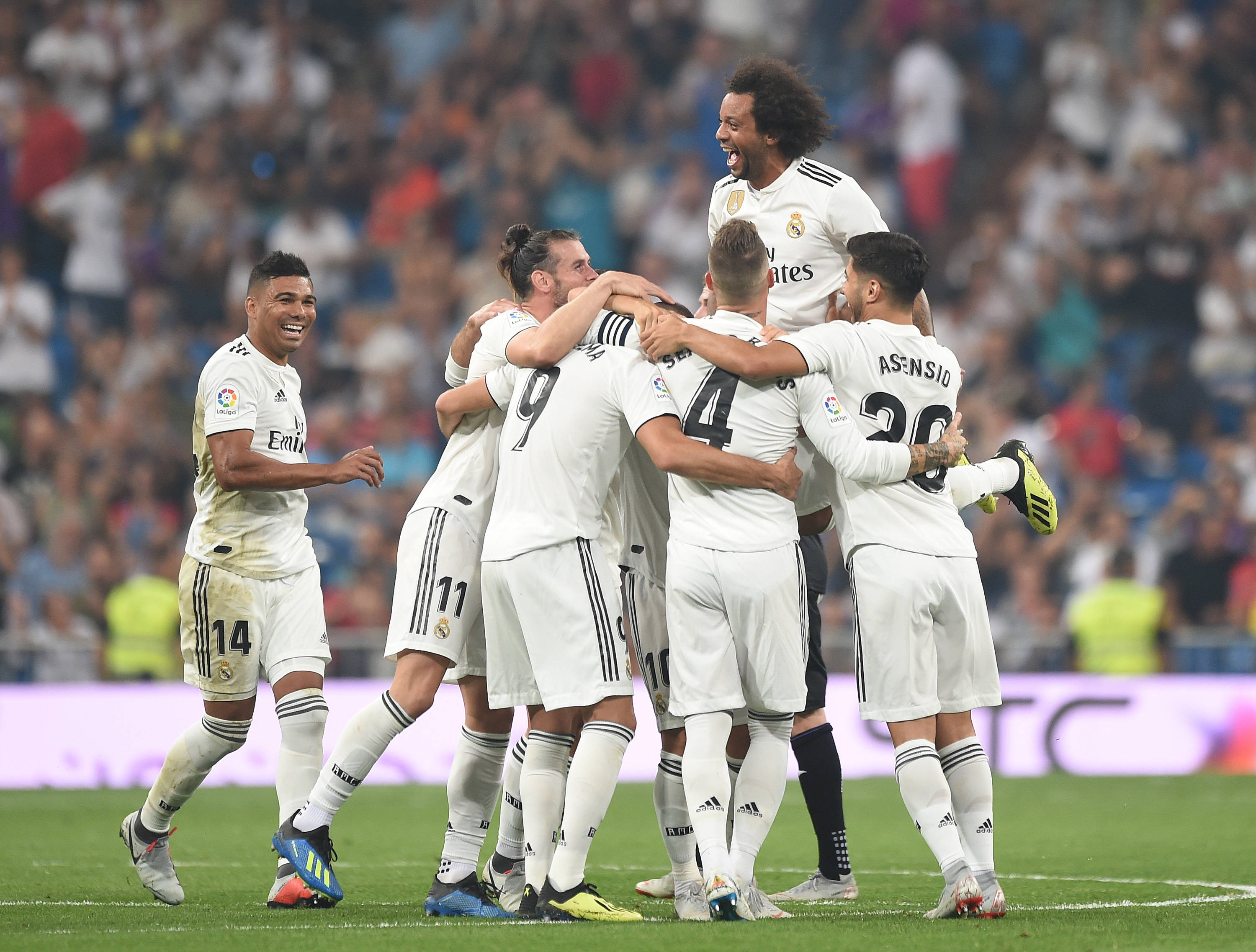 Real Madrid 4K 桌布 壁紙 — 皇家馬德里足球員身穿白色球衣，在球場燈光下於充滿活力的綠色草地上以喜悅的擁抱慶祝進球。