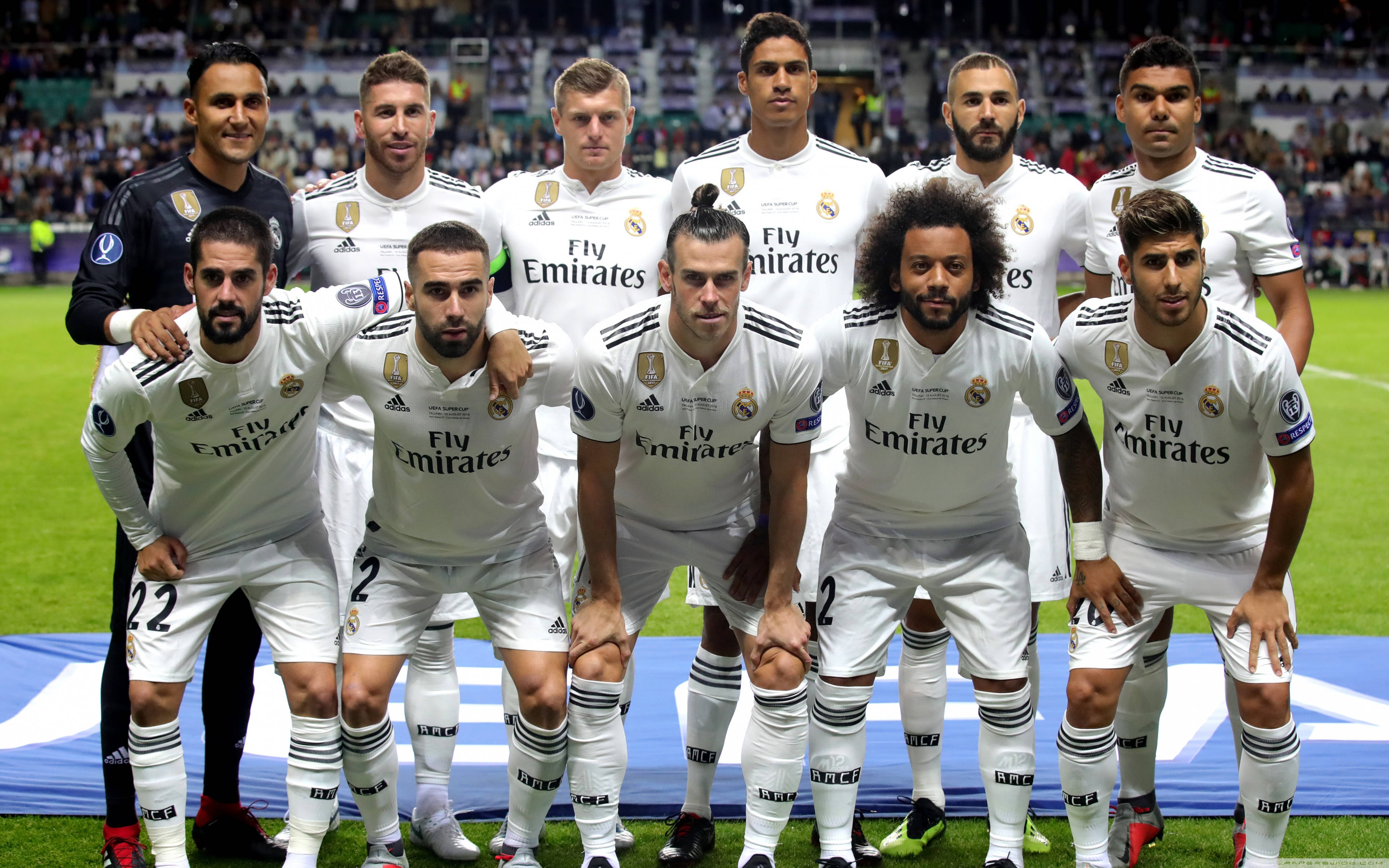 Real Madrid 4K 桌布 壁紙 — 皇家馬德里足球隊在體育場燈光下，身穿白色球衣在充滿活力的綠色球場上擺姿勢。
