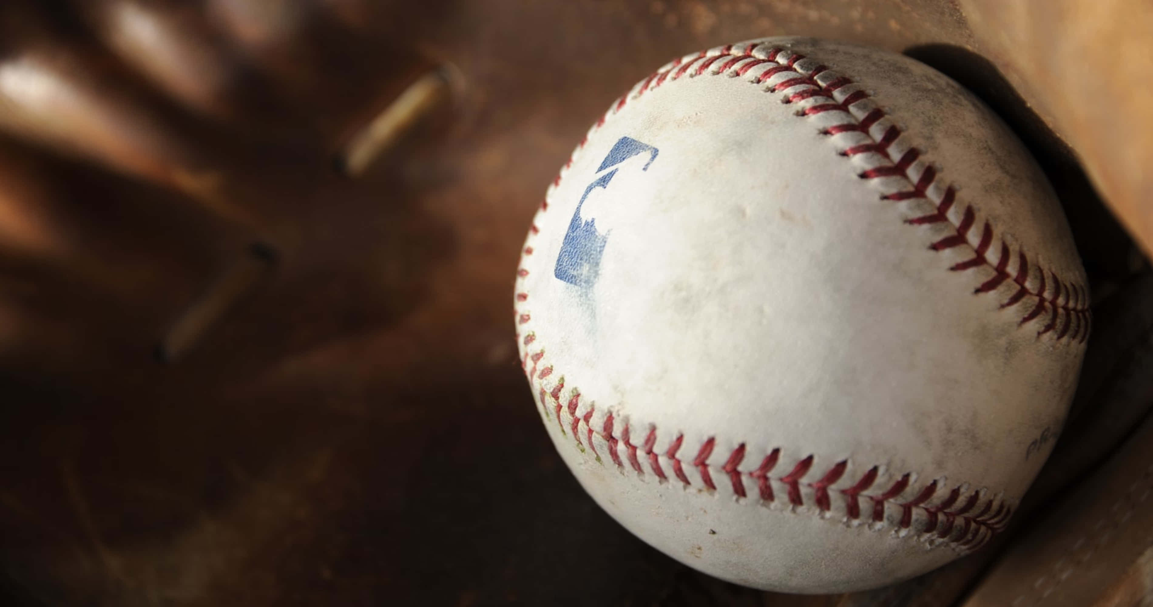 Awesome Baseball 桌布 壁紙 — 皮革手套內一顆帶有紅色縫線的磨損棒球的特寫。