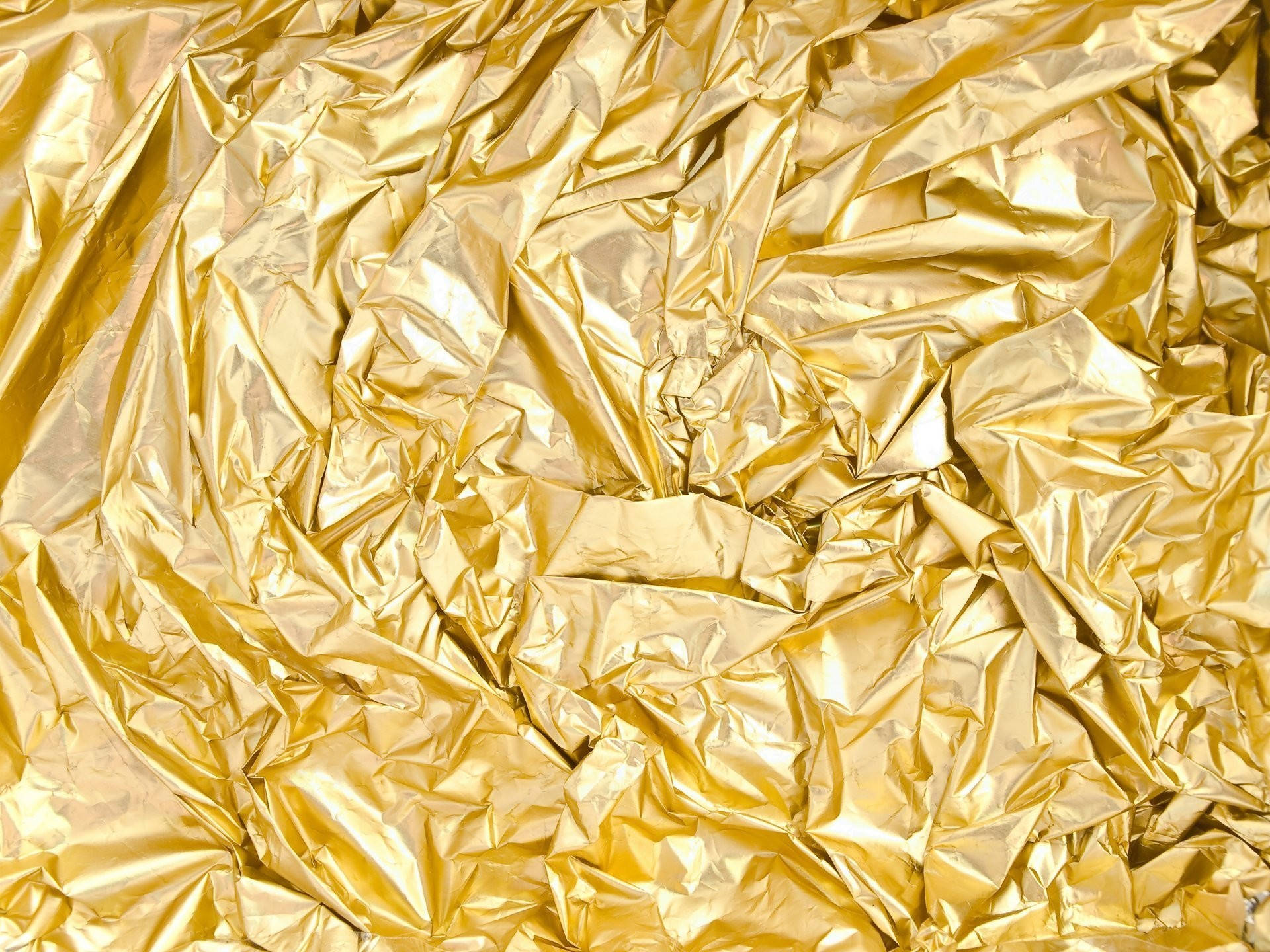 Foil 桌布 壁紙 — 皺巴巴的金箔特寫，帶有閃亮摺痕，在紋理圖案中反射光線。
