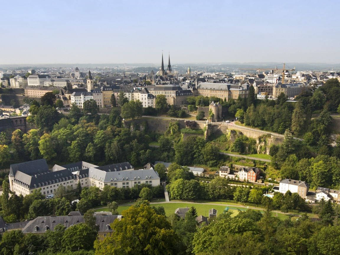 Luxembourg 桌布 壁紙 — 盧森堡市的鳥瞰圖，歷史建築和茂密的綠樹在晴朗的藍天下。