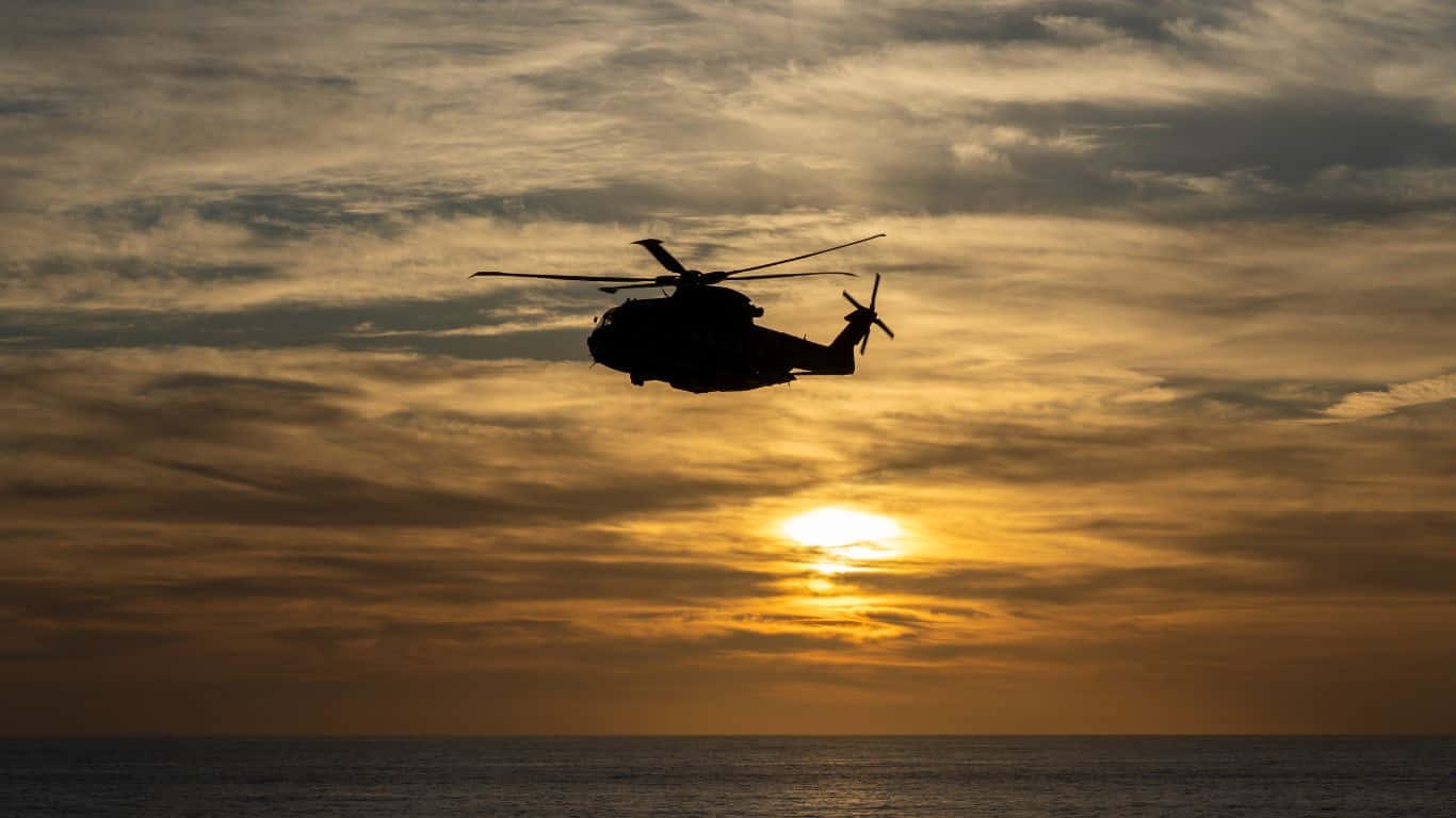 1366x768 Helicopters 桌布 壁紙 — 直升機的剪影在平靜的海面上，襯著金黃色的日落天空翱翔。