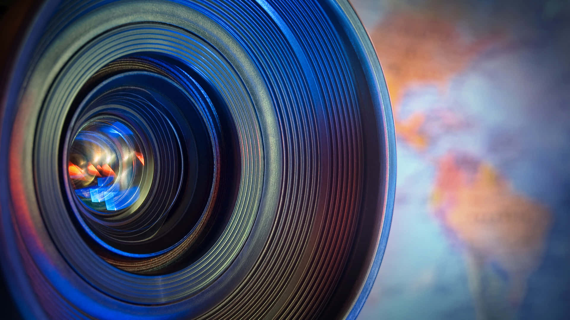 Camera Lens 桌布 壁紙 — 相機鏡頭特寫，帶有鮮豔的藍色和橙色反射，背景中顯現模糊的世界地圖。