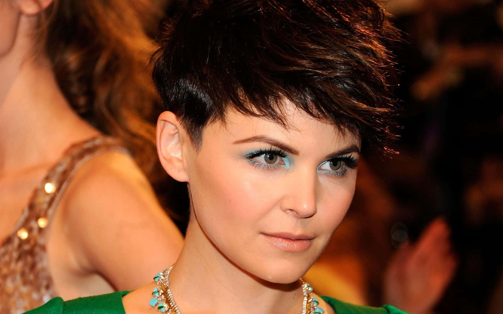 ginnifer goodwin 桌布 壁紙 — 短黑髮、搶眼藍色眼影的女性，身穿綠色上衣和綠松石項鍊的特寫肖像。