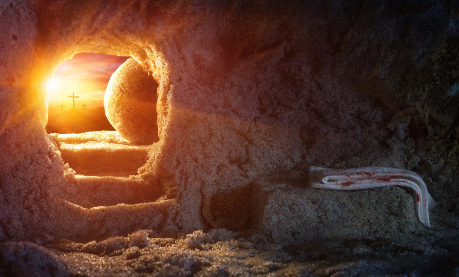 Resurrection 桌布 壁紙 — 石墓入口顯露一個發光的日出，遠處有十字架，階梯旁有一塊沾血布料。