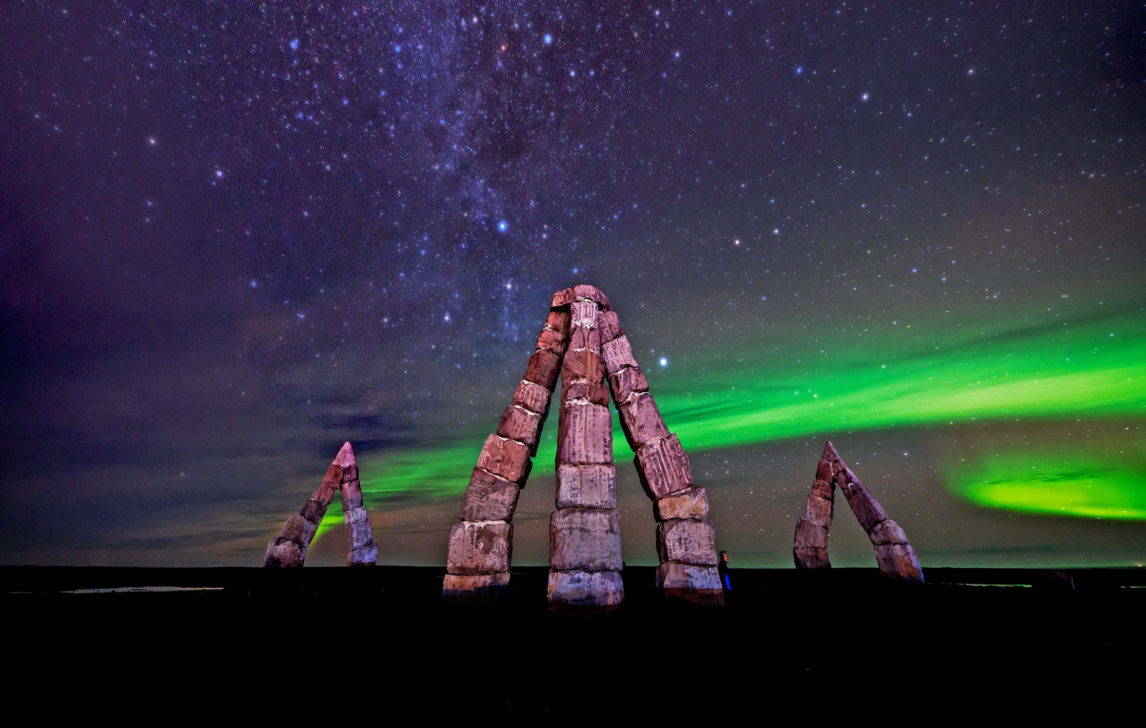 aurora borealis 桌布 壁紙 — 石柱在星空下巍然聳立，充滿活力的綠色北極光在上方舞動。