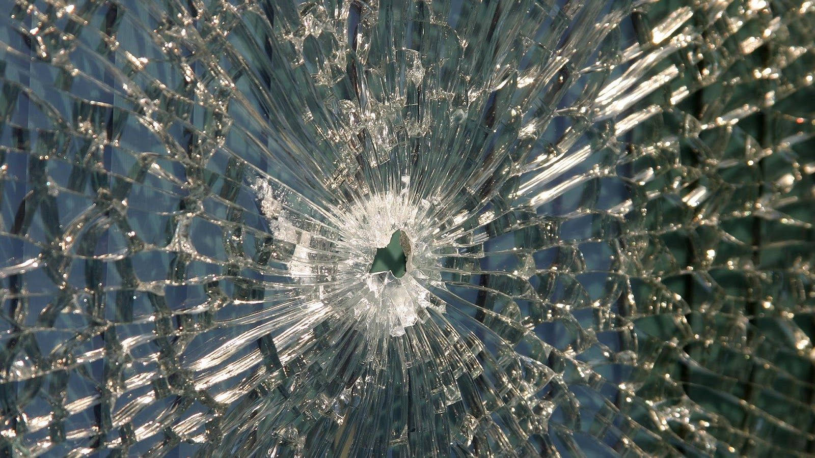 cracked 桌布 壁紙 — 破碎玻璃的特寫，中央撞擊點在模糊的藍色背景上散發出尖銳裂紋。