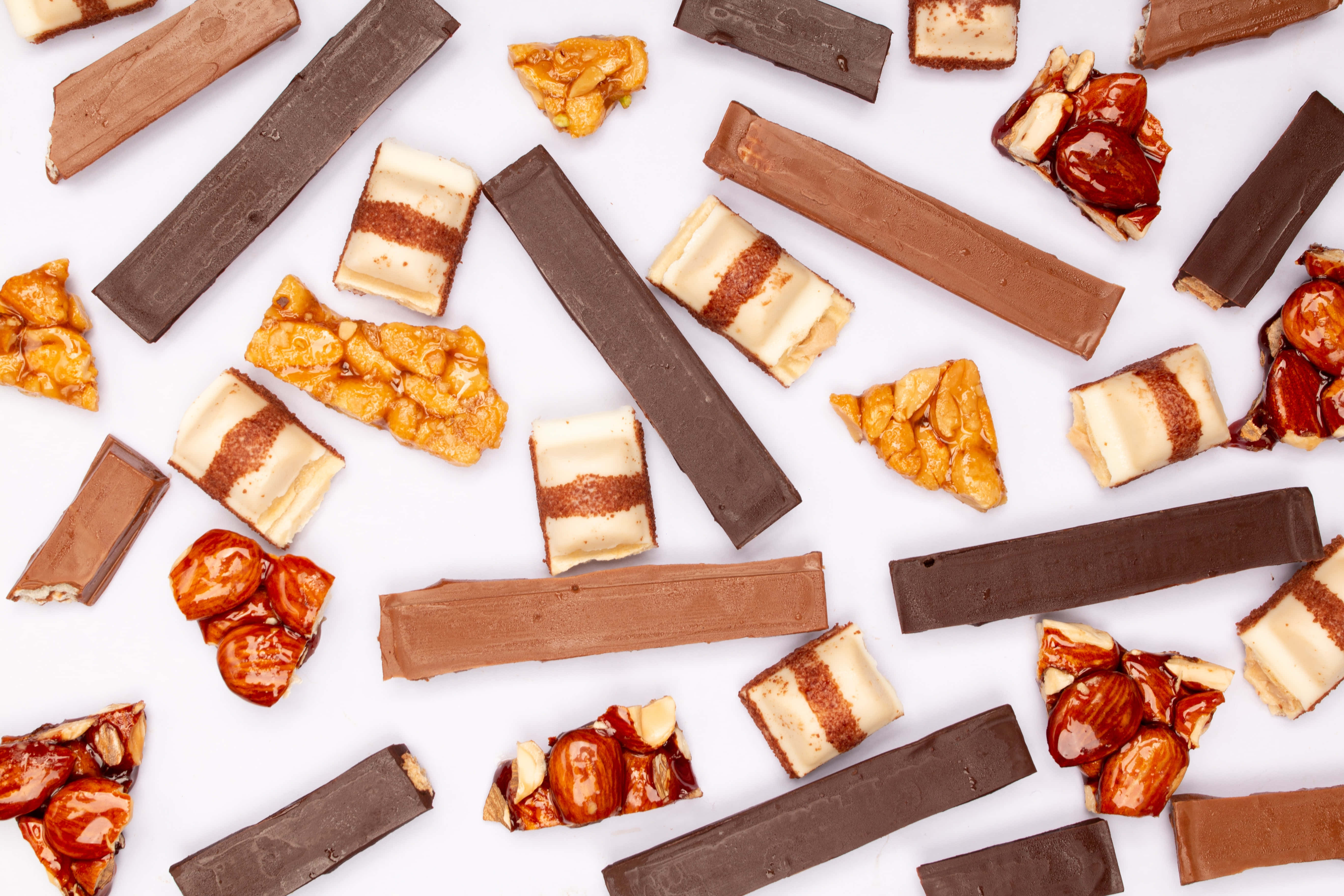 Caramel 桌布 壁紙 — 破碎的巧克力條和焦糖杏仁簇散落在明亮的白色表面上。