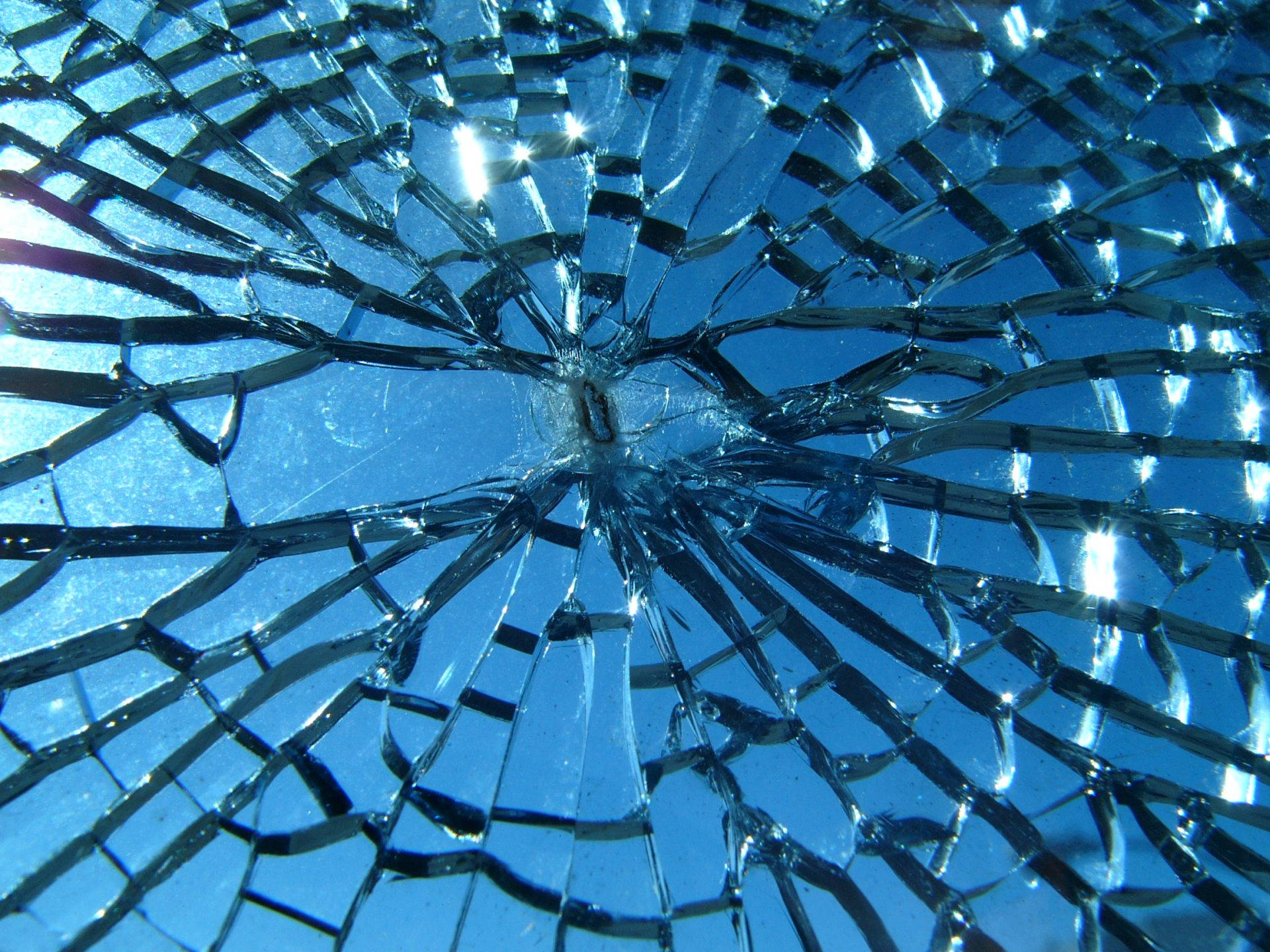 Screen 桌布 壁紙 — 破碎的玻璃表面，尖銳裂紋向外擴散，背景是充滿活力的藍天。