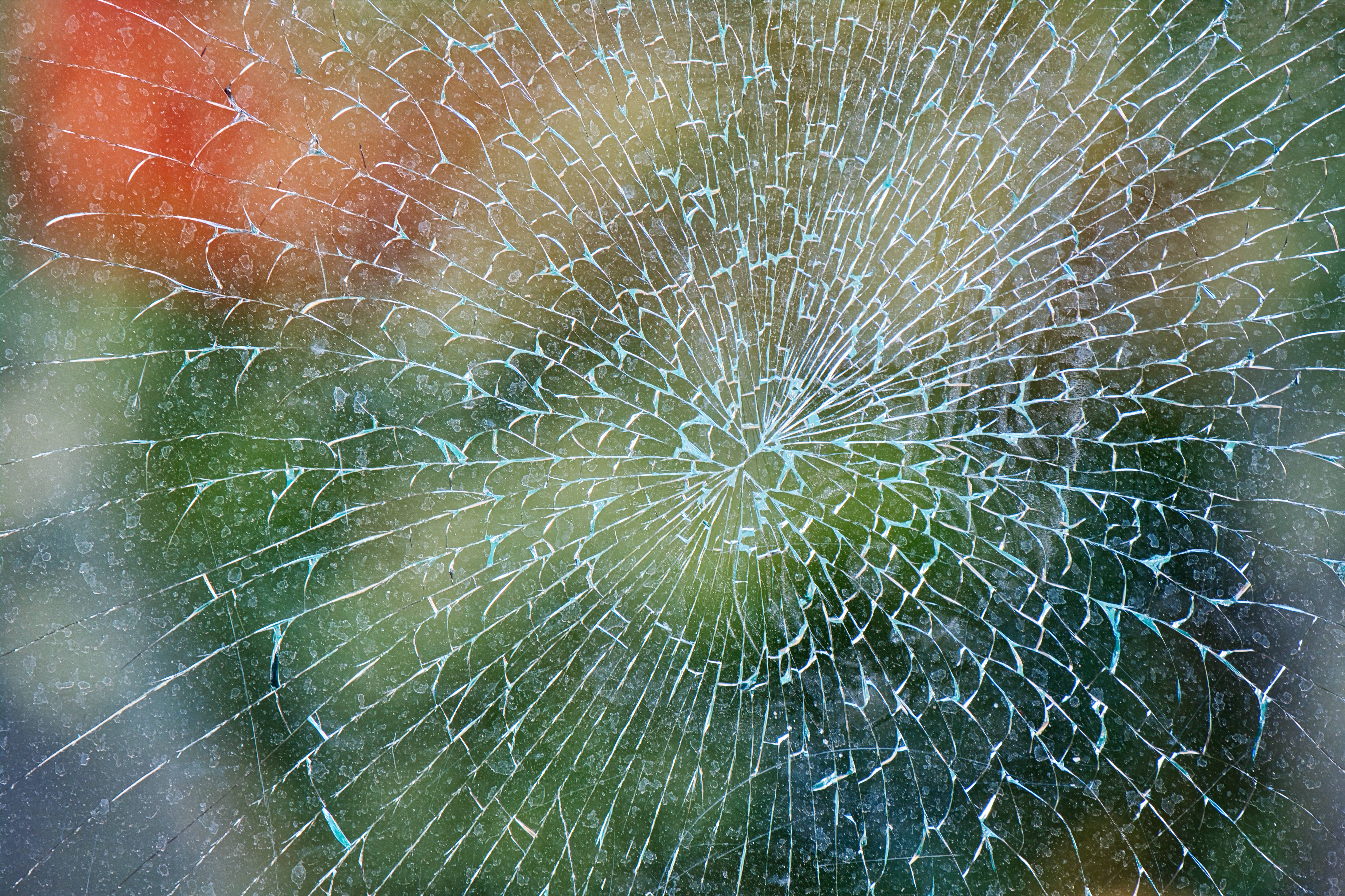 Broken 桌布 壁紙 — 破碎的玻璃表面，從中心撞擊點放射出徑向裂紋，背景為模糊的彩色。