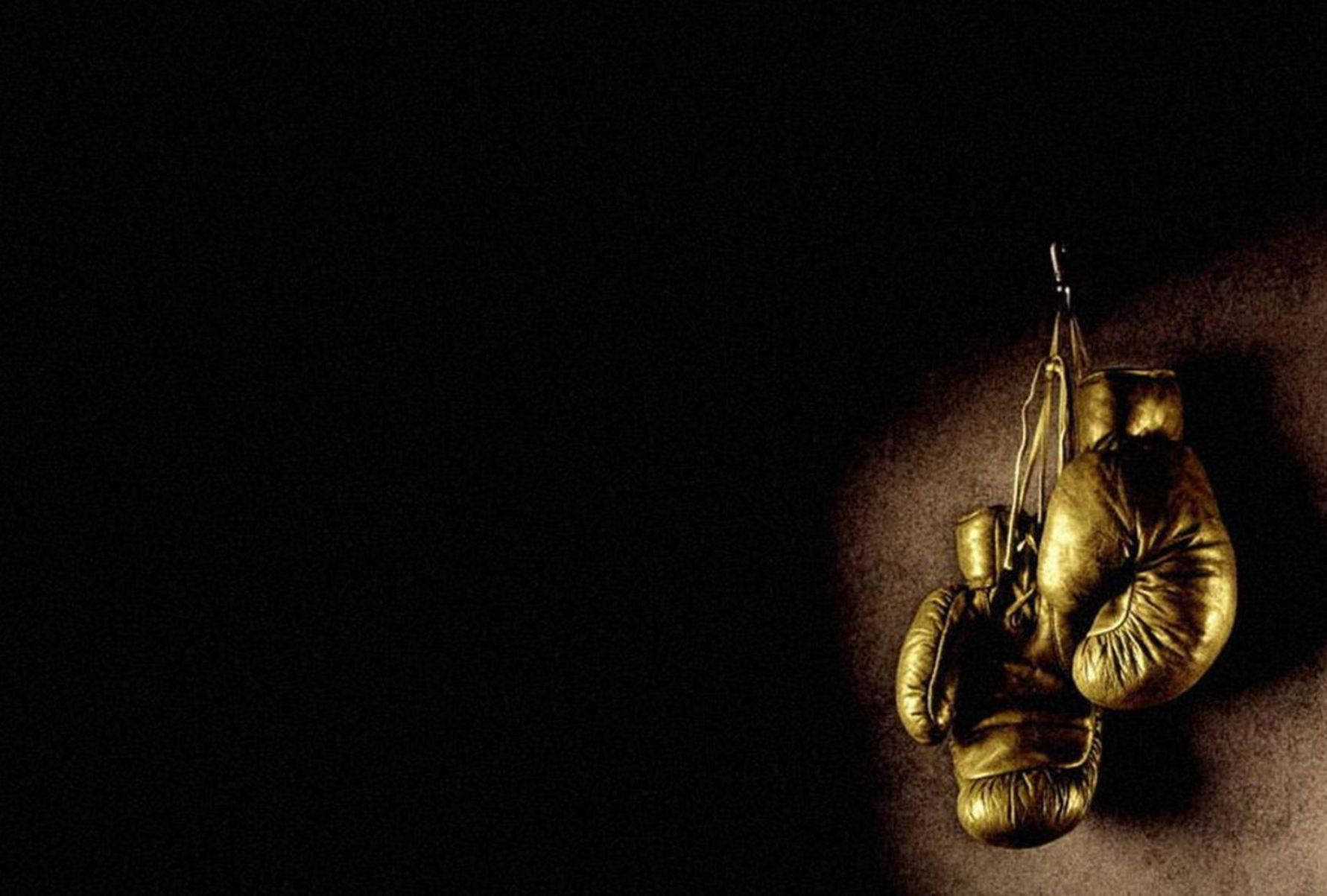Boxing 桌布 壁紙 — 破舊的金色拳擊手套懸掛在深沉的陰影中，被一道戲劇性的聚光燈照亮。