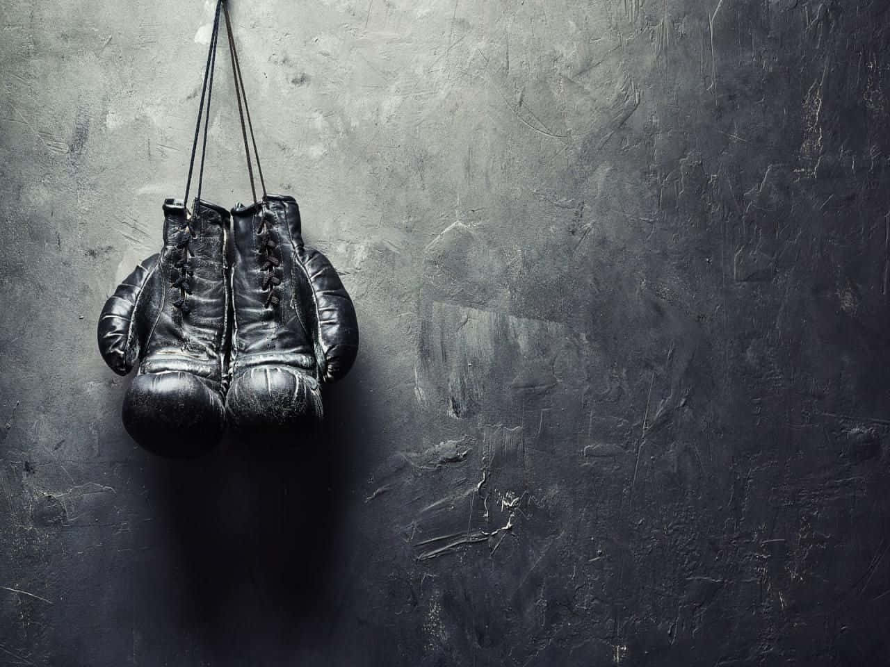 Boxing 桌布 壁紙 — 破舊的黑色拳擊手套用鞋帶掛在粗糙紋理的灰色牆上，投下深深的陰影。