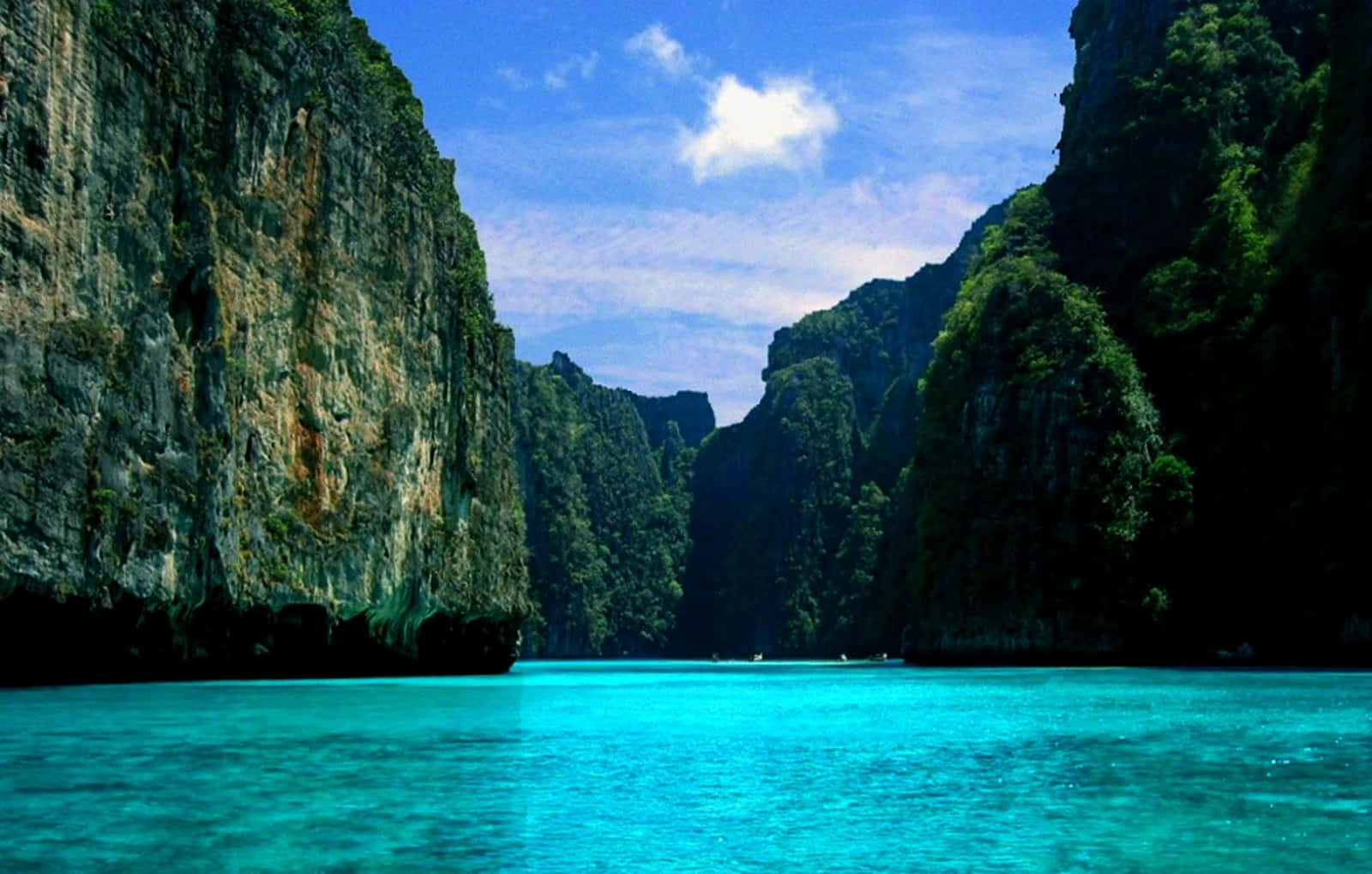 screensaver 桌布 壁紙 — 碧綠色的海水位於高聳的叢林覆蓋的石灰岩懸崖之間，在明亮的藍天下有零星雲朵。