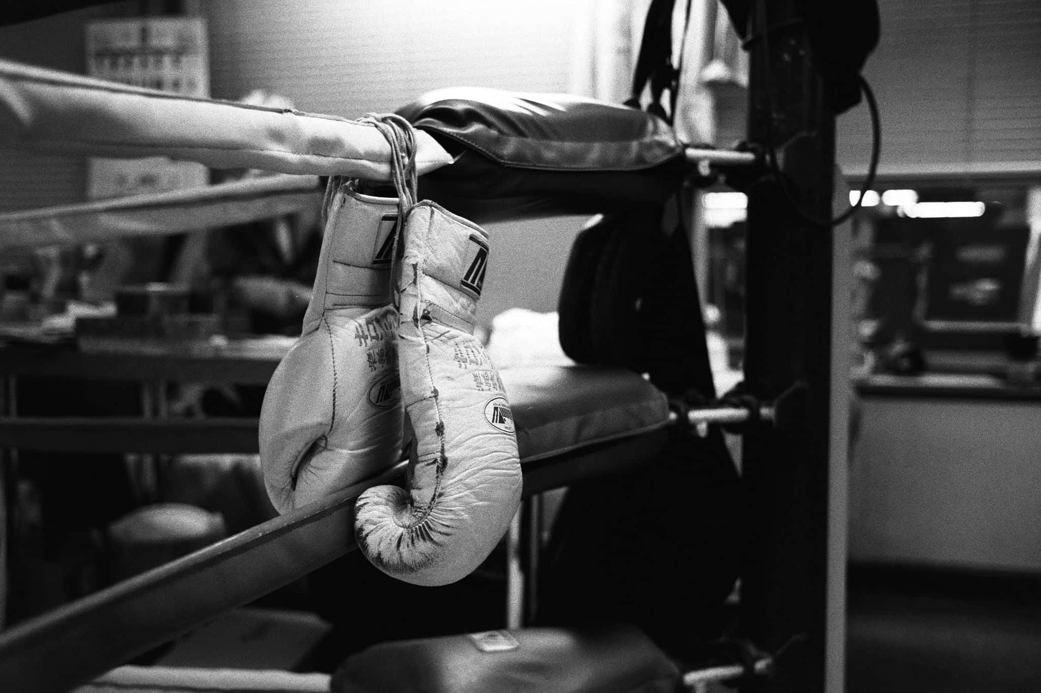 Boxing 桌布 壁紙 — 磨損的拳擊手套掛在昏暗健身房的擂臺繩索上，喚起堅韌的決心和運動歷史。