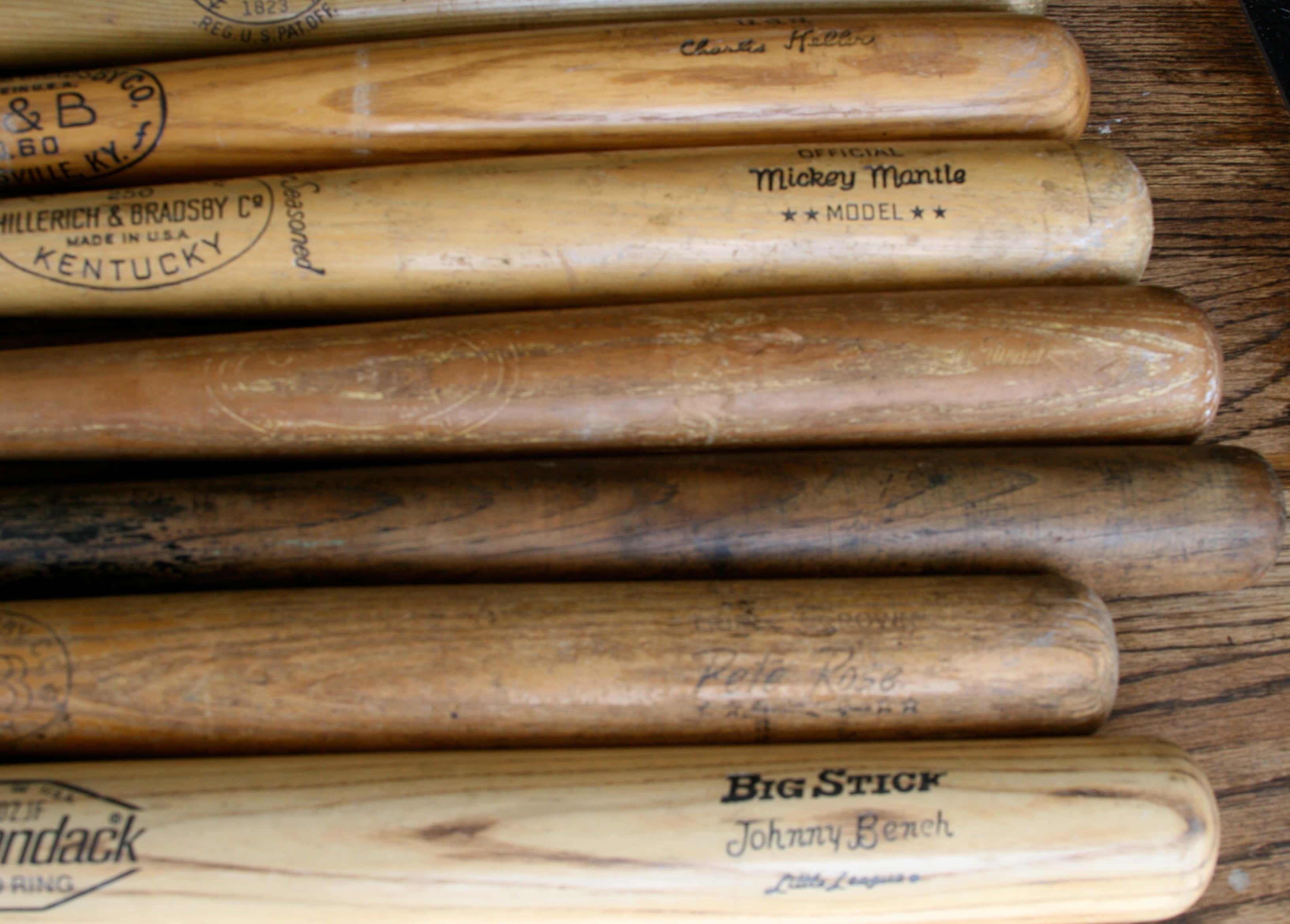 baseball bat 桌布 壁紙 — 磨損的木製棒球棒，上面有復古球員名字和品牌，整齊地排列在質樸的木質表面上。