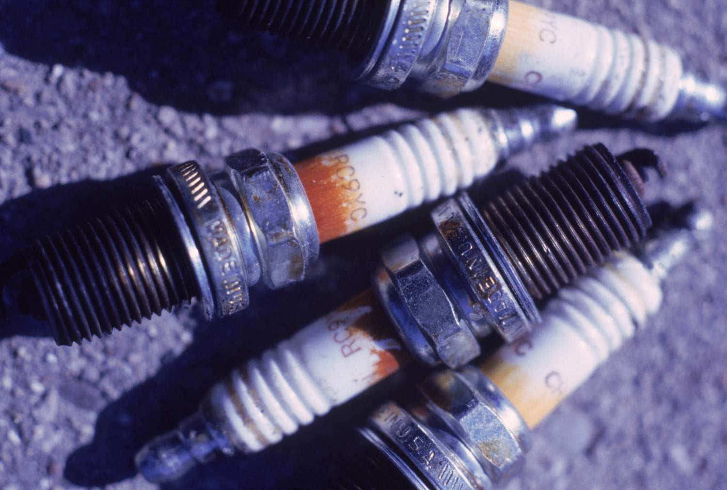 Spark Plug 桌布 壁紙 — 磨損的火星塞帶有橙色沉積物，散落在佈滿砂礫的瀝青上，在冷藍色燈光下。