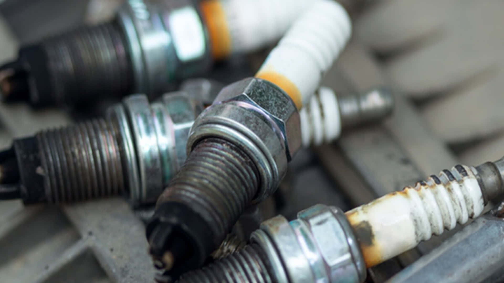 Spark Plug 桌布 壁紙 — 磨損的火星塞特寫，帶有碳積聚和腐蝕，放置在金屬表面上。