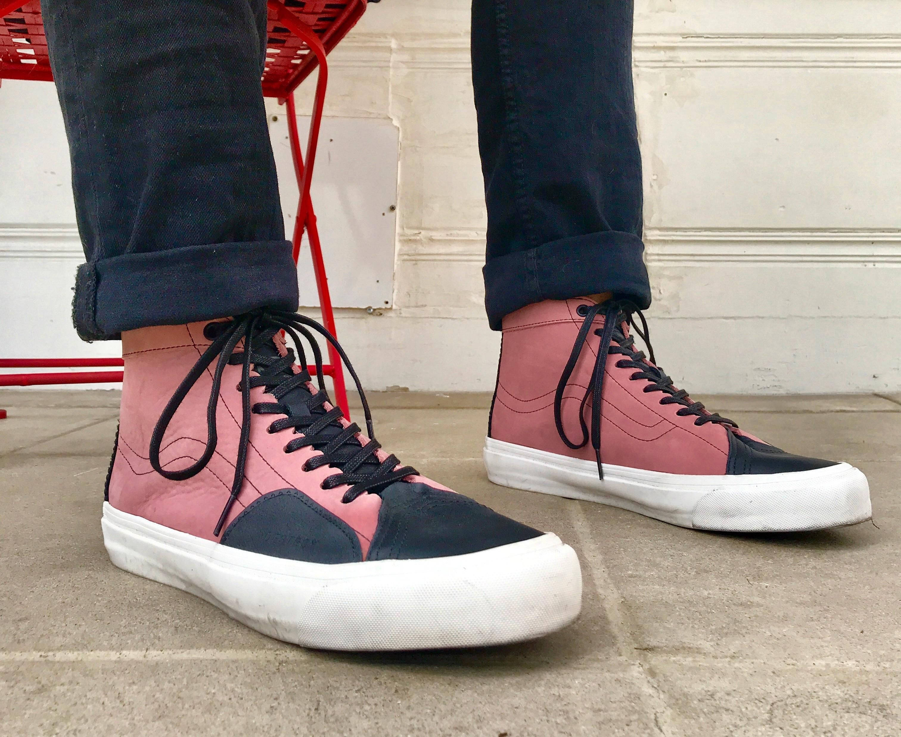 Vans Off The Wall 桌布 壁紙 — 磨損的粉紅色和深藍色高筒運動鞋特寫，白色鞋底，放在混凝土上，旁邊有紅色椅子和白色牆壁。