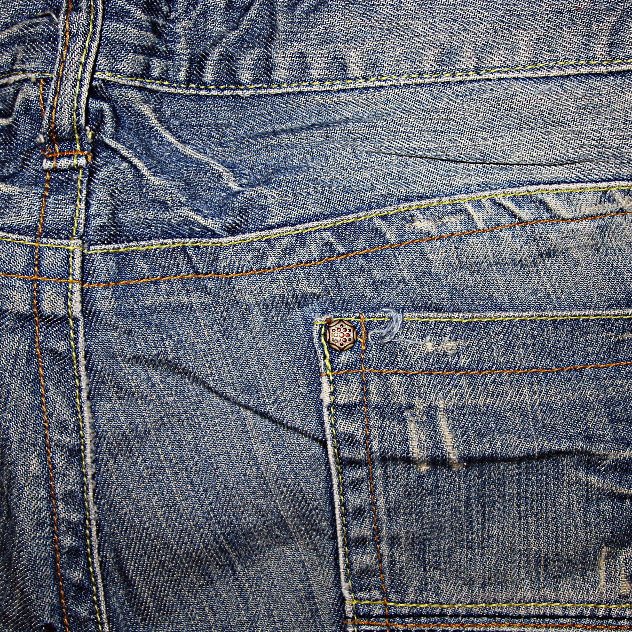 Denim 桌布 壁紙 — 磨損的藍色牛仔褲特寫，顯示後袋上的詳細縫線和六角形鈕扣。