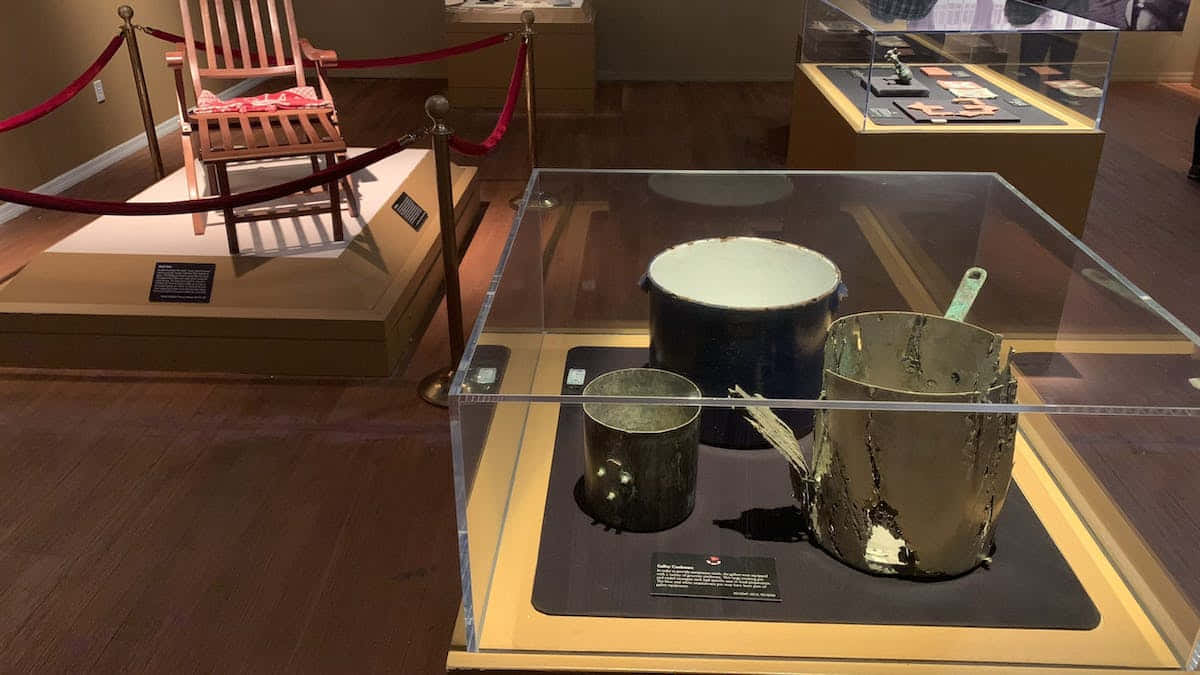 Titanic 桌布 壁紙 — 磨損的金屬鍋和平底鍋陳列在博物館展覽的玻璃櫃中，展廳有木地板和用繩索隔開的展示區域。