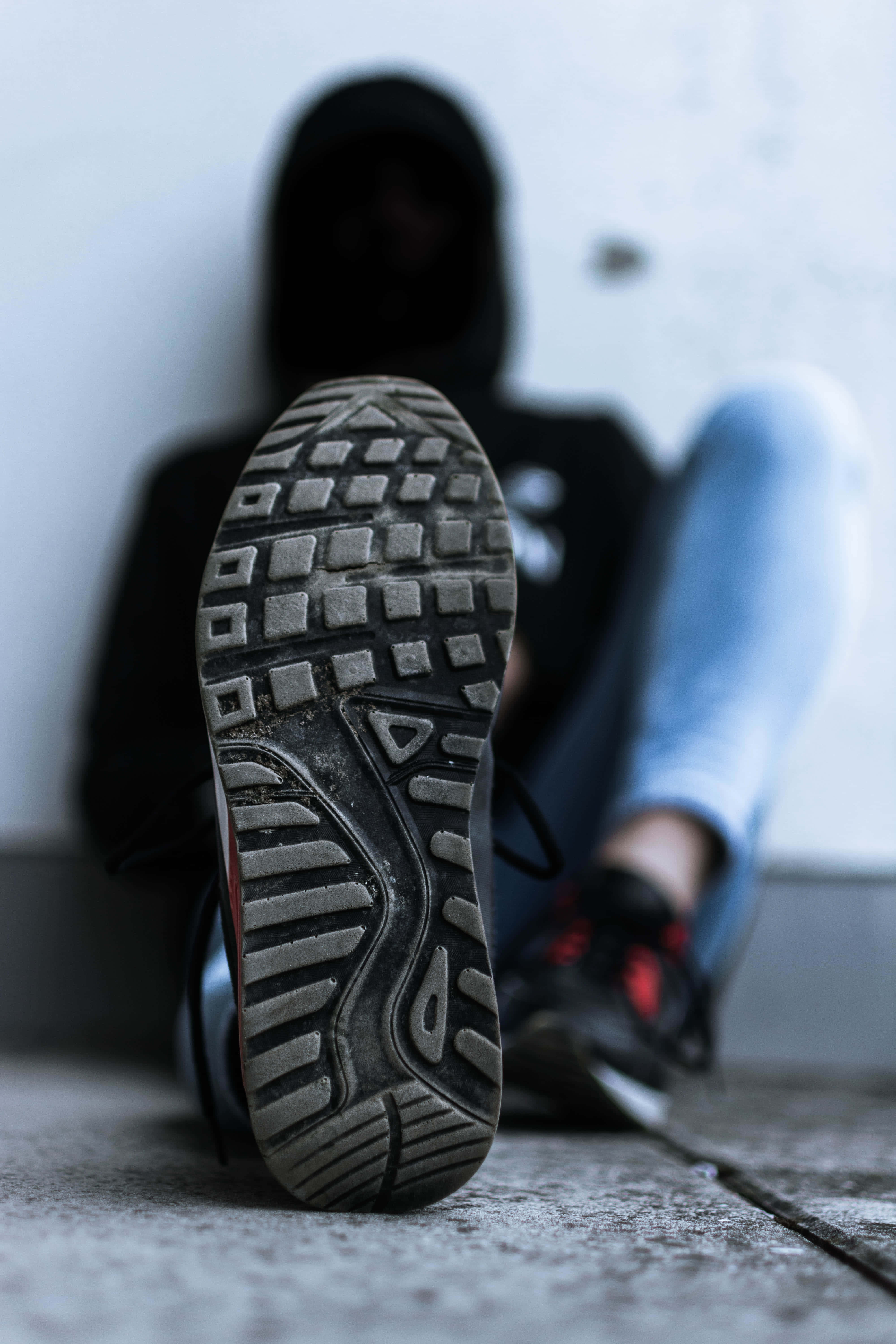 Shoe 桌布 壁紙 — 磨損運動鞋鞋底的特寫，背景是一個穿著黑色連帽衫的模糊身影坐在混凝土地板上。