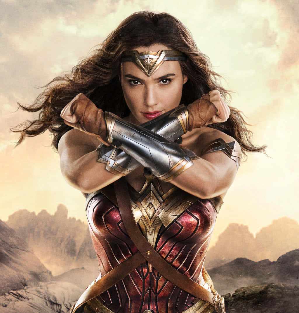 Wonder Woman 桌布 壁紙 — 神力女超人以她標誌性的盔甲，在朦朧的山脈背景下，交叉雙臂，帶著兇猛的目光，挑釁地站立著。