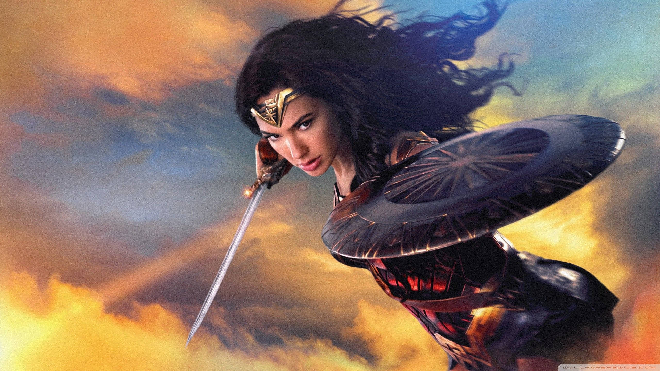 Wonder Woman 1984 桌布 壁紙 — 神力女超人用動態戰鬥姿勢揮舞劍和盾牌，背景是熾熱的日落雲彩。