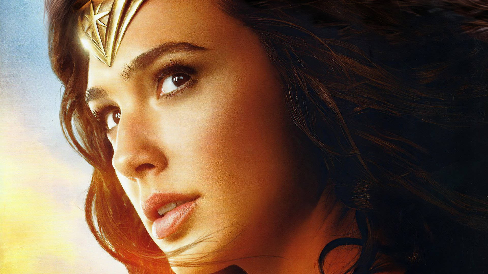 Gal Gadot 桌布 壁紙 — 神力女超人的近距離特寫，頭戴金色頭飾，秀髮飄逸，背景是明亮的天空。