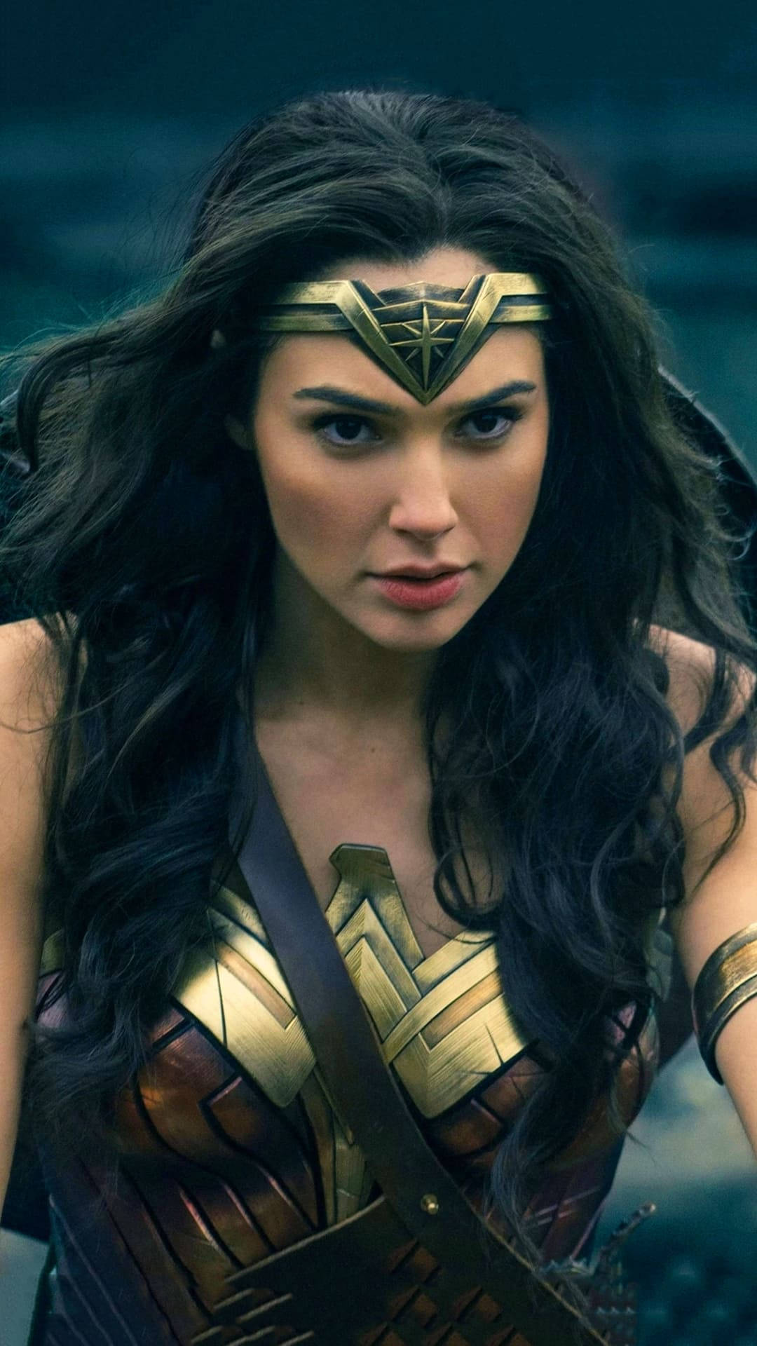 Wonder Woman 桌布 壁紙 — 神力女超人穿著金色盔甲，黑髮飄逸，在模糊的藍綠色背景下凝視著。