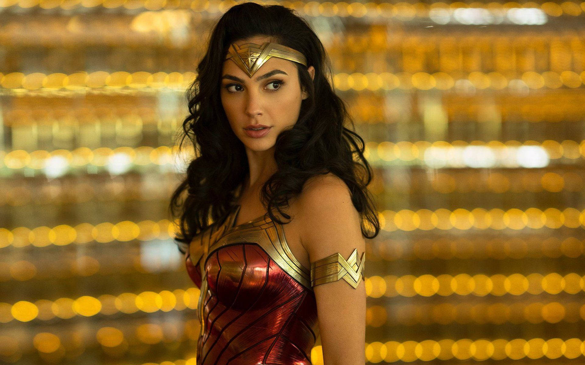 Wonder Woman 1984 桌布 壁紙 — 神力女超人自信地站在閃爍的金色散景背景前，身穿紅色和金色的盔甲服裝。